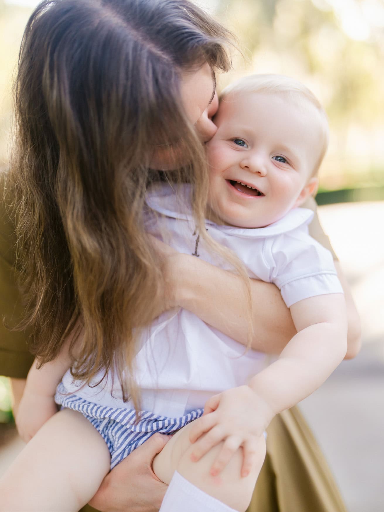 Joyful mother holding smiling baby boy outdoors, capturing candid family moments during sunny day at the park. Perfect for family beach portraits, capturing genuine happiness and love.