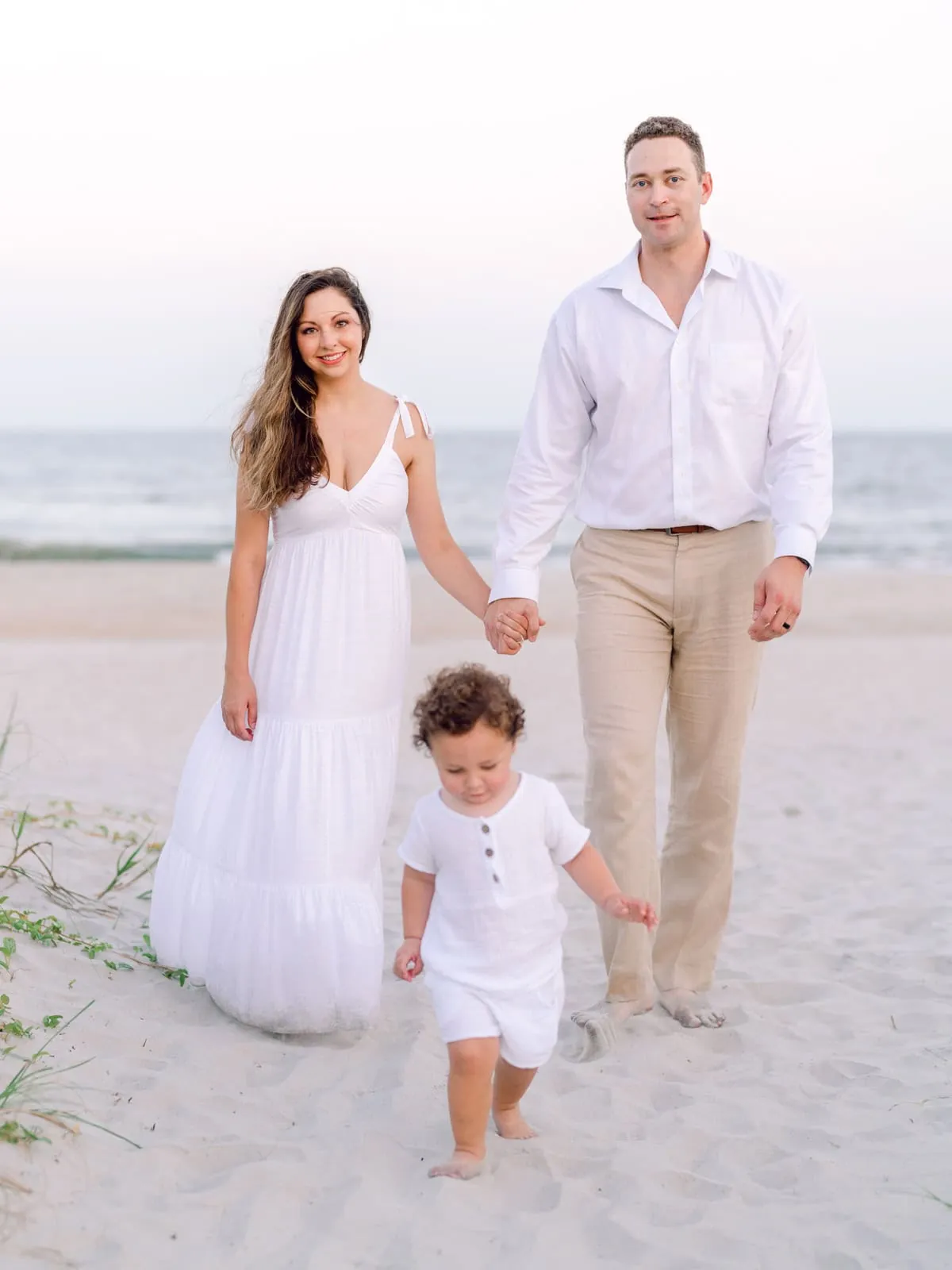 Family wearing coordinated all white outfits during a beach family photo session at sunset