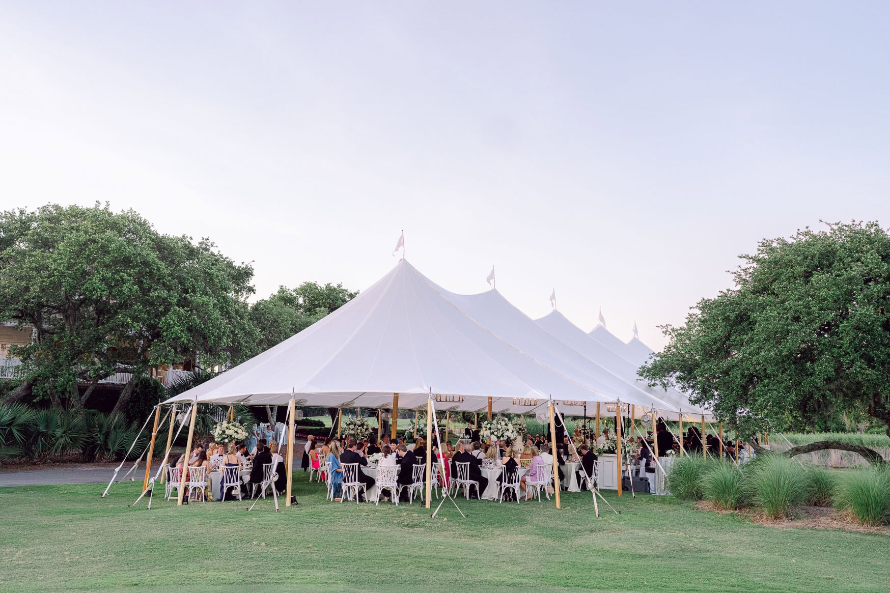 Vibrant wedding reception under a large white tent on lush green lawn with elegant table settings and floral arrangements. Perfect for outdoor wedding photography capturing joyful moments and celebration atmosphere.