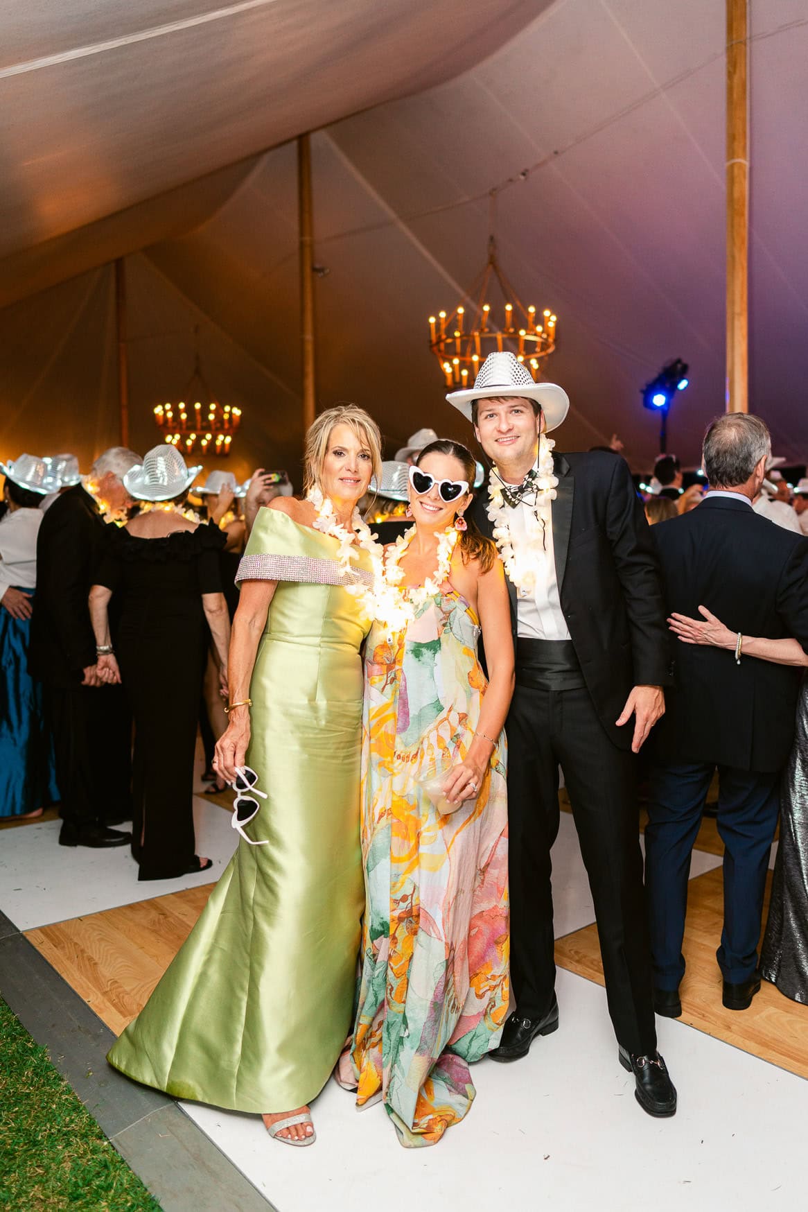 Colorful wedding guests in tropical attire with leis and fun accessories at a lively celebration in an elegant tent.