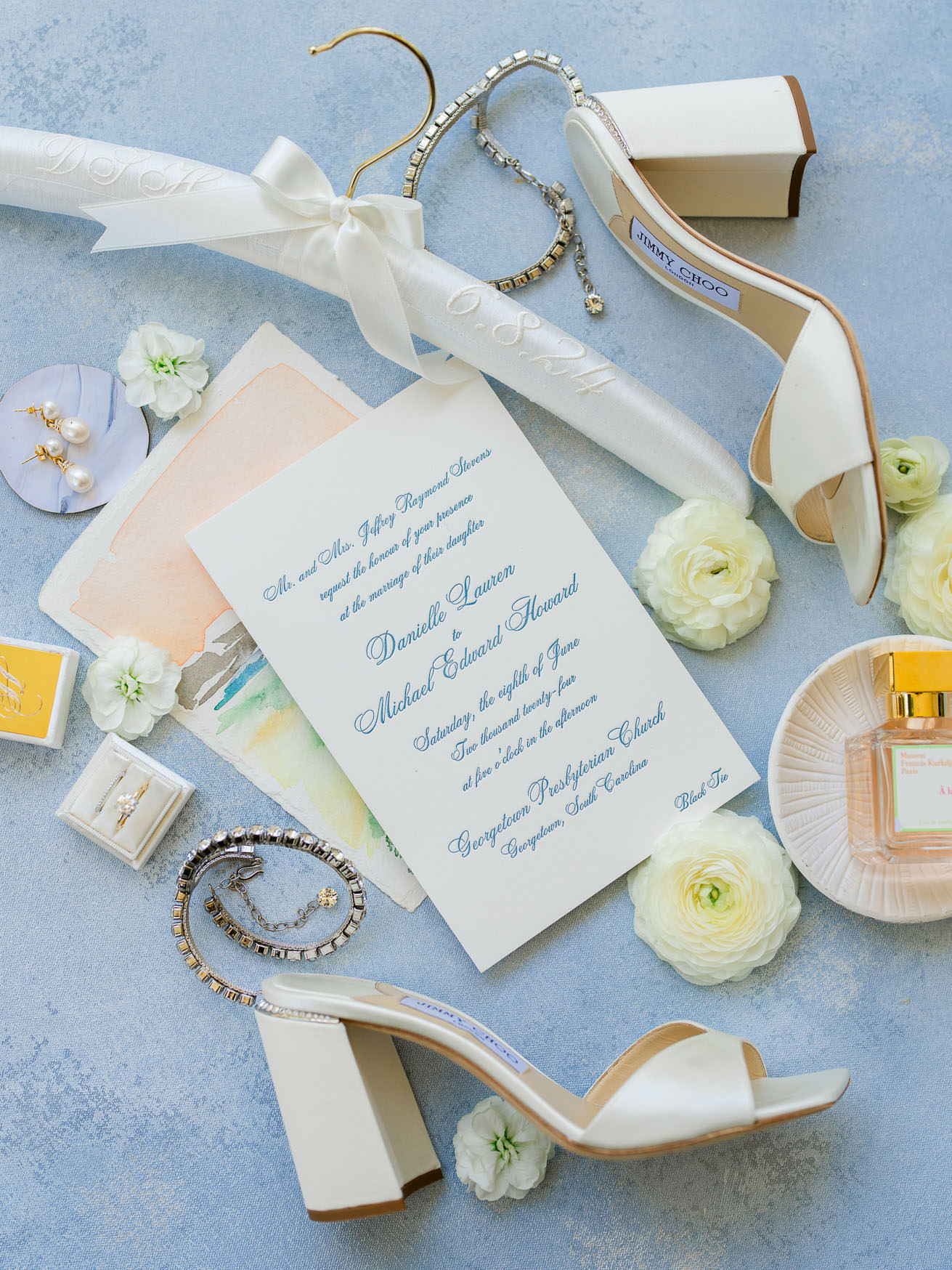 Elegant wedding invitation with white heels, jewelry, and flowers for bride and groom.