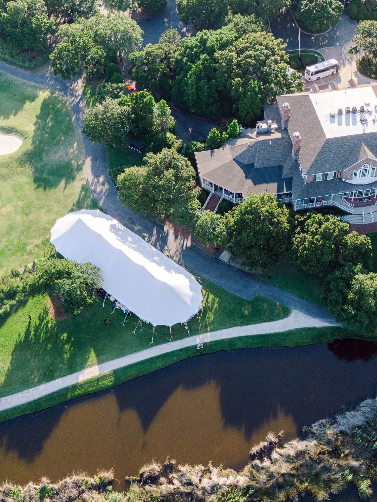 Aerial view of a large house with surrounding trees, a pond nearby, and an event tent set up on the lawn, perfect for capturing outdoor wedding or family celebrations.