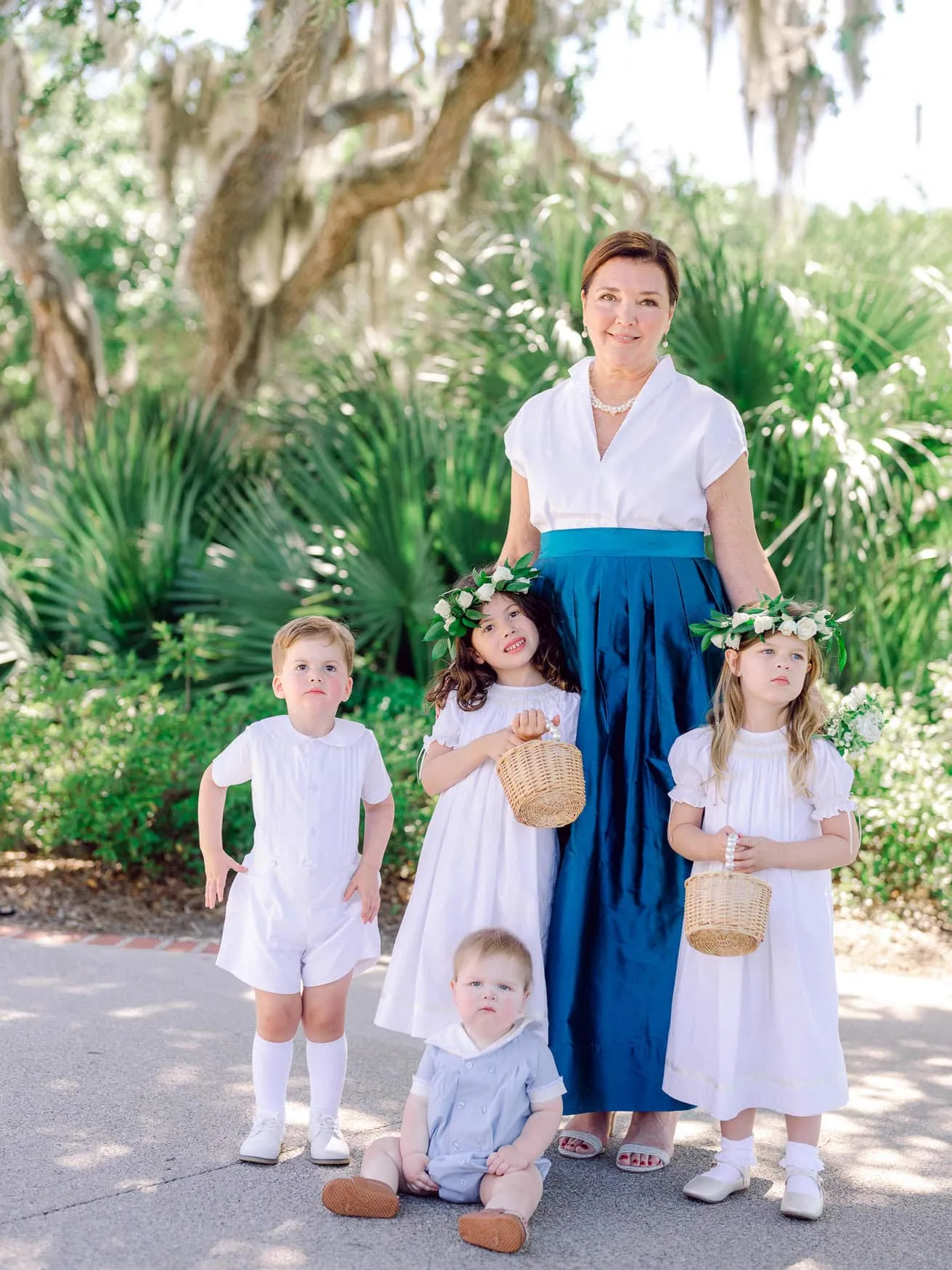 Bright outdoor family portrait featuring a mother with her young children in white dresses and floral crowns during a sunny day. Perfect for wedding and family beach photography sessions.