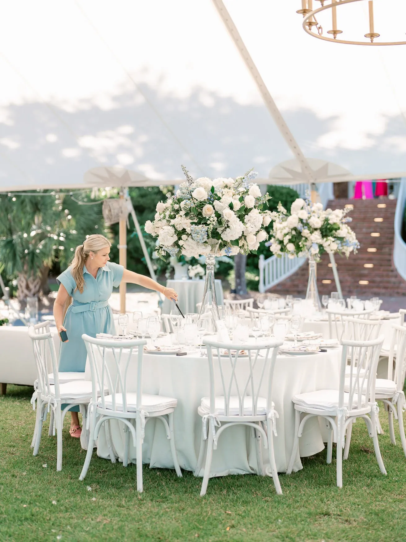 Elegant outdoor wedding reception setup with tall floral centerpieces and white chairs under a canopy, perfect for romantic garden weddings.
