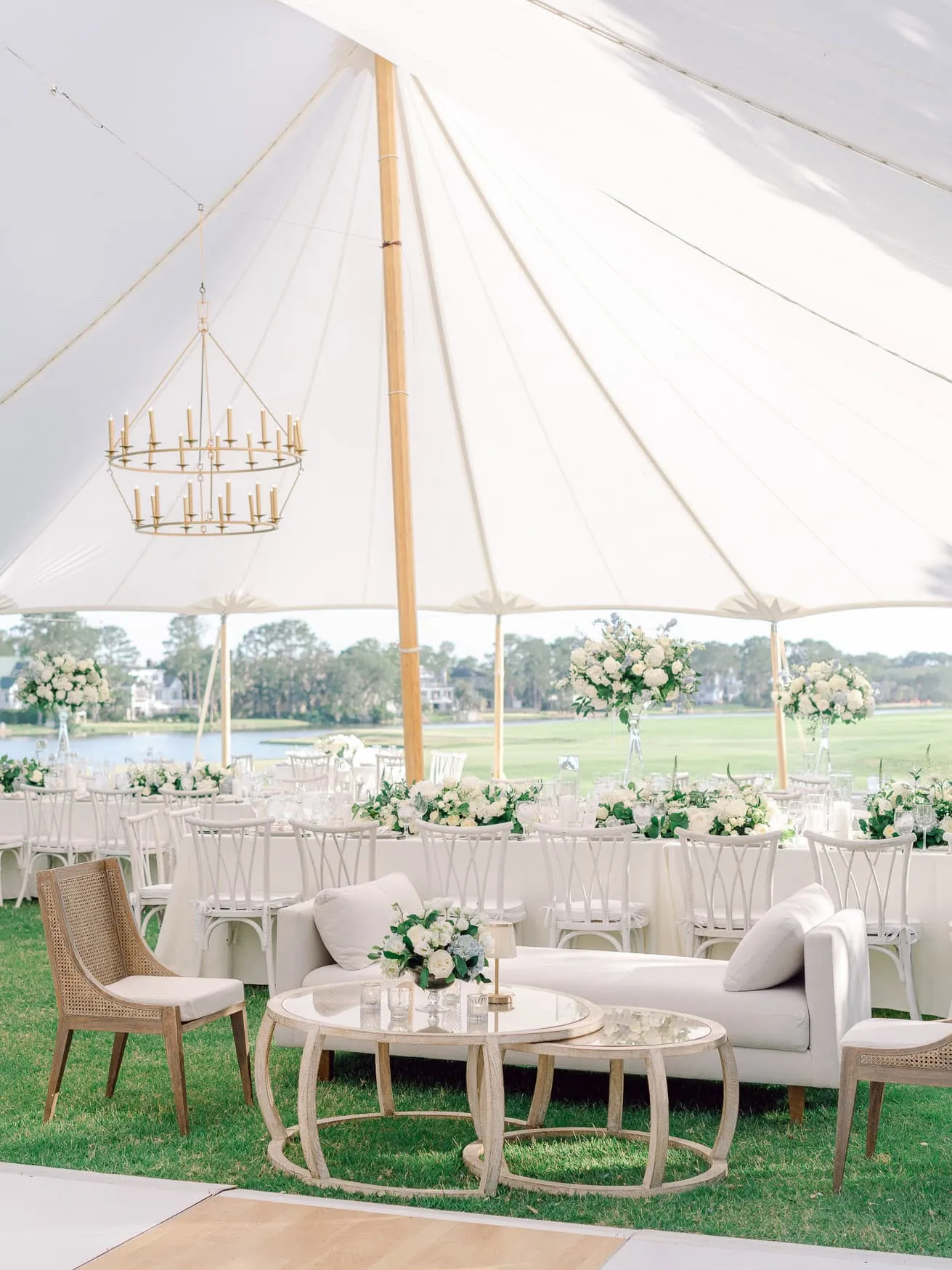Elegant outdoor wedding reception under a large white tent with floral decor and sophisticated seating arrangements, perfect for capturing romantic and joyful moments. | Beautifully decorated outdoor wedding reception in a white tent with elegant floral arrangements and stylish seating, set against a picturesque water and green landscape, ideal for wedding photography and special event coverage.