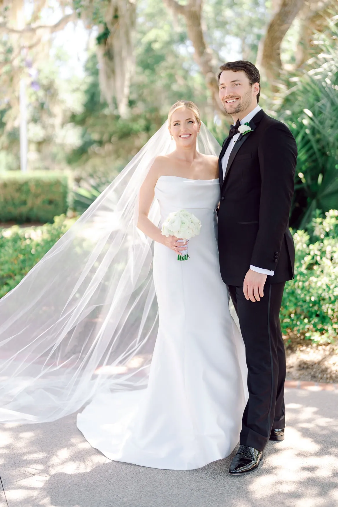 Elegant wedding portrait of a bride and groom outdoors with lush greenery, capturing timeless love and celebration moments in natural sunlight, perfect for wedding photography portfolio.