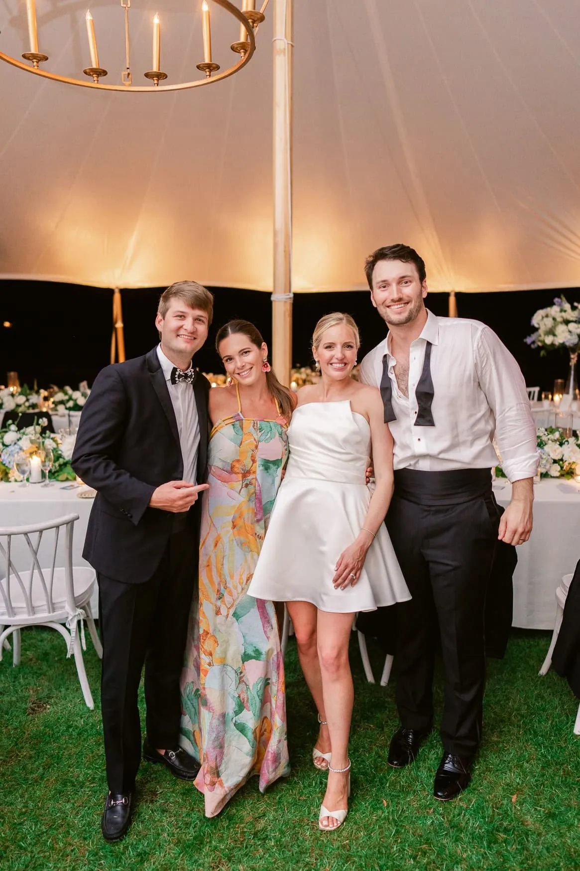 Elegant wedding portrait of smiling newlyweds with friends under a luxury tent, showcasing professional wedding photography, evening celebration, and joyful atmosphere.