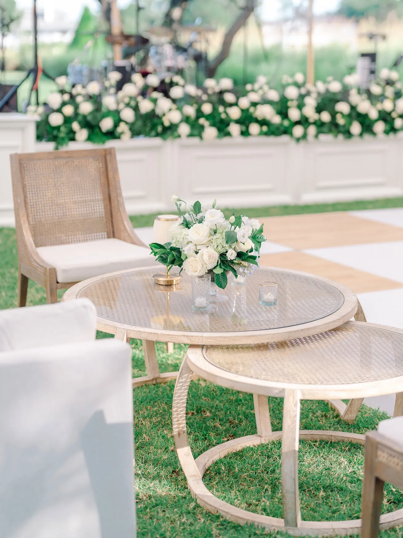 Elegant wedding reception setup with round wooden tables, white floral centerpieces, and cozy seating arrangements on a lush green lawn. Perfect for outdoor wedding photography.