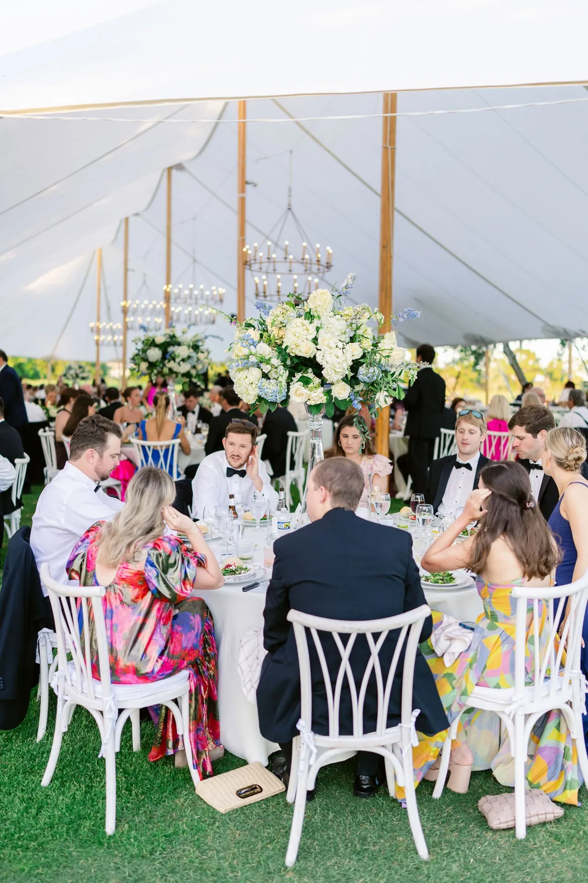 Elegant wedding reception under a large white tent with floral centerpieces and chandeliers, capturing joyful guests celebrating at a luxurious outdoor wedding.