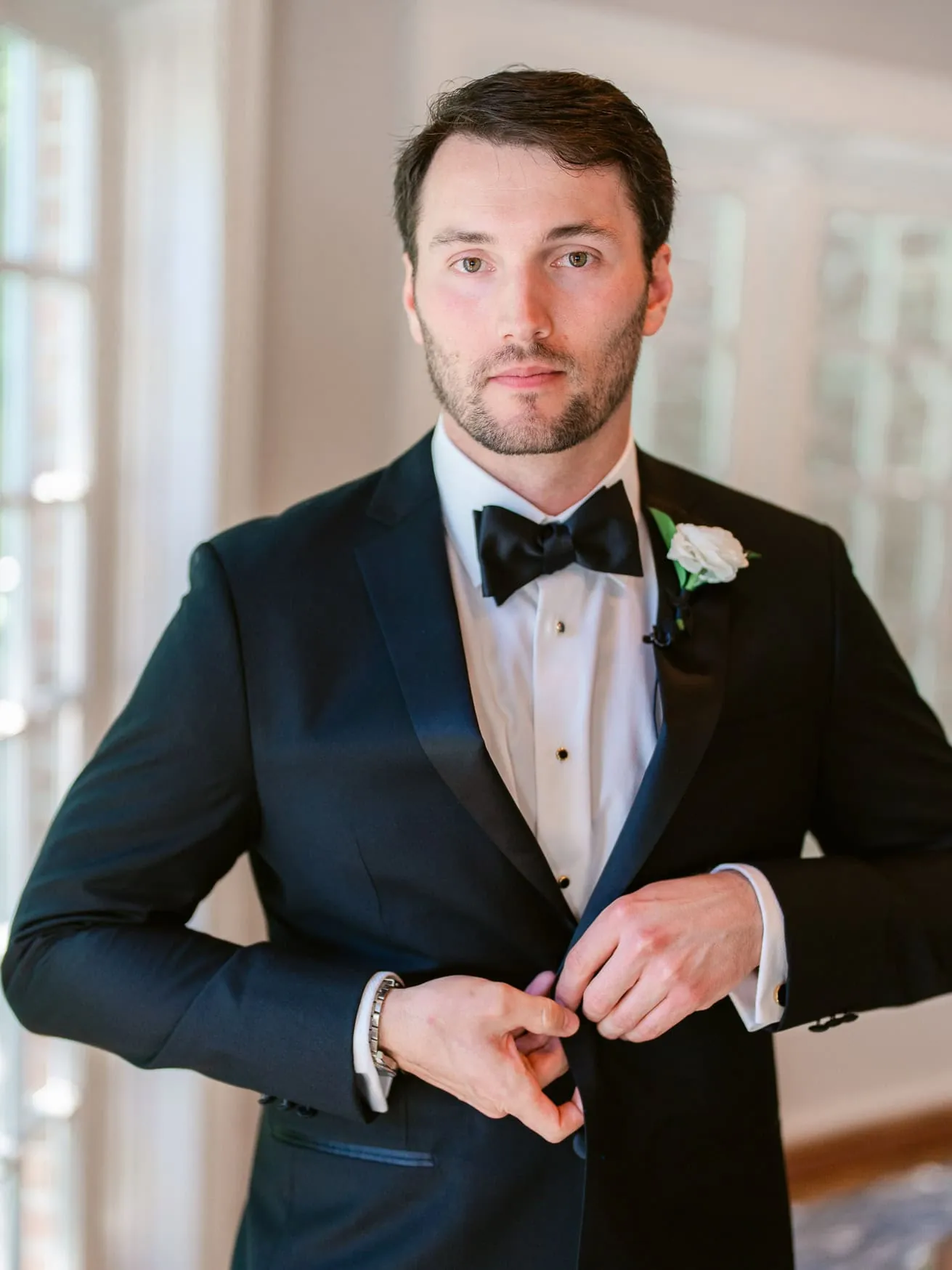 Groom in black tuxedo adjusting cuffs for wedding portrait during wedding day.