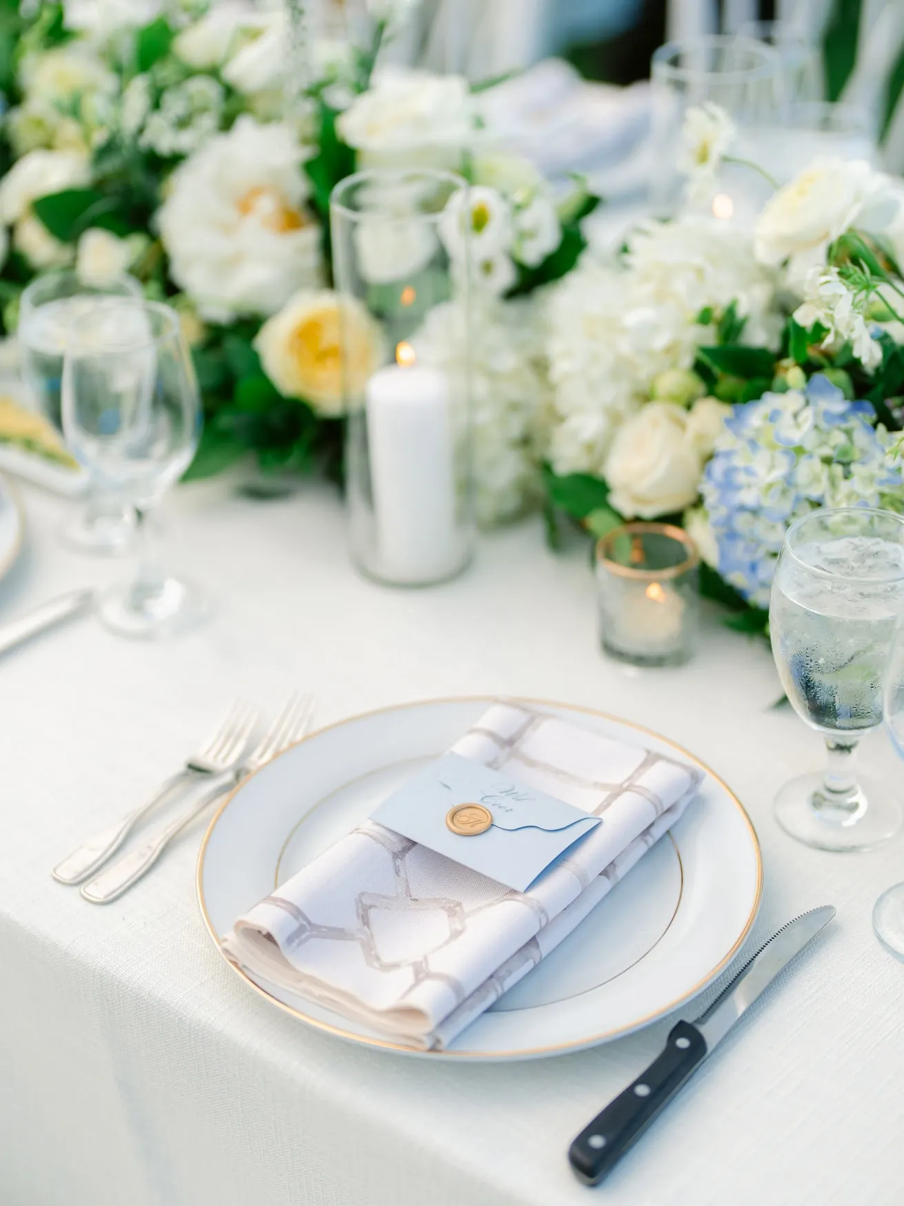 Vegan wedding table setting with white floral centerpiece, elegant white dinnerware, and gold accents, perfect for a romantic and sophisticated wedding reception.