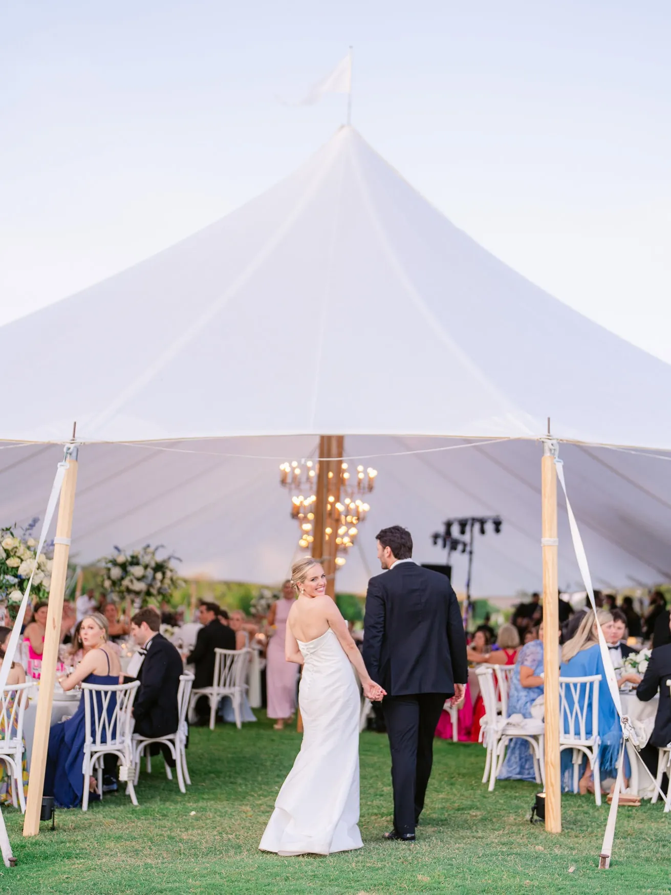 Vibrant wedding photo capturing bride and groom dancing under a large white wedding tent outdoor celebration.