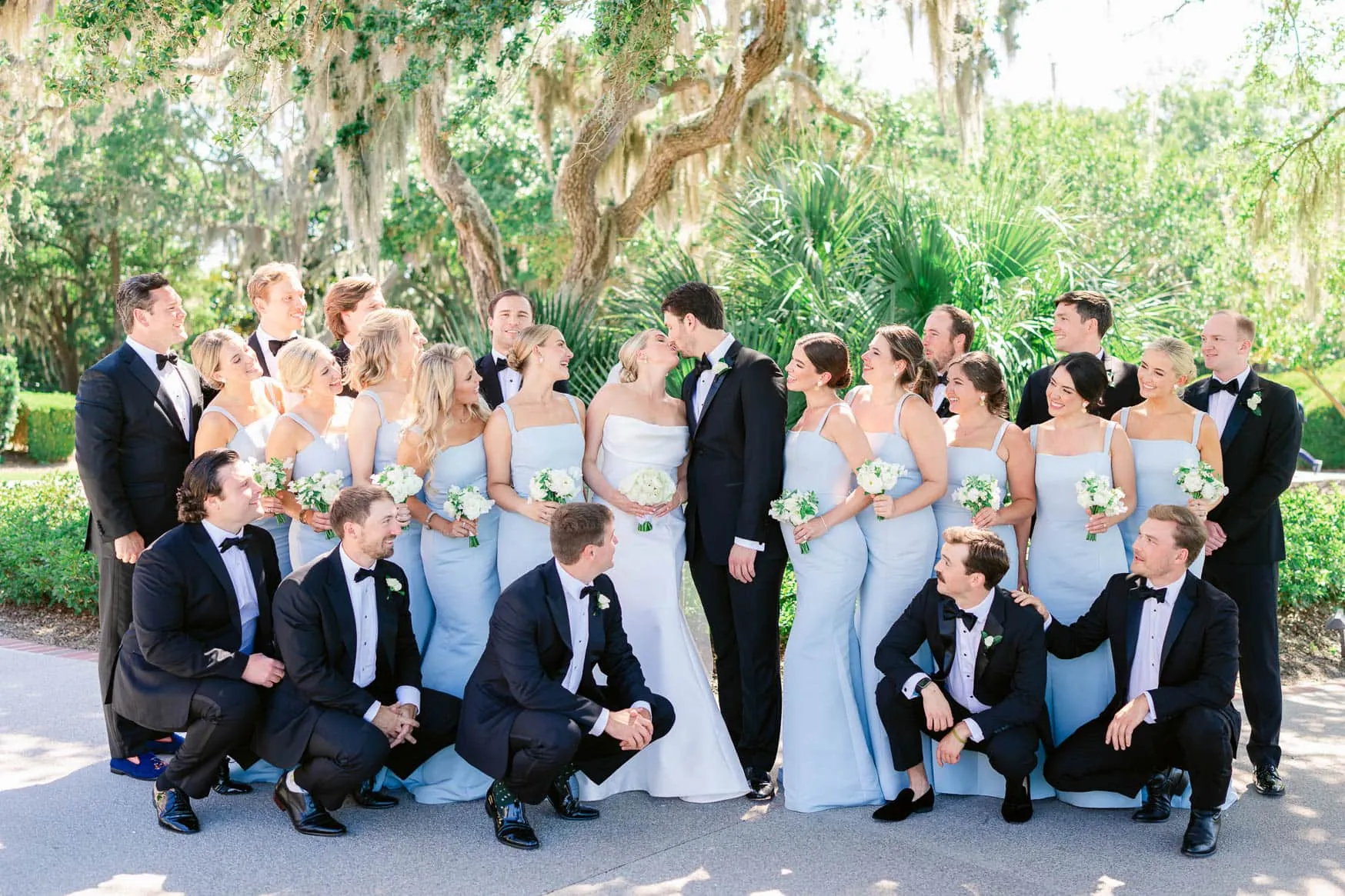 Vibrant wedding photography of a bride and groom surrounded by their wedding party in an outdoor garden setting, capturing joyful moments and elegant attire.