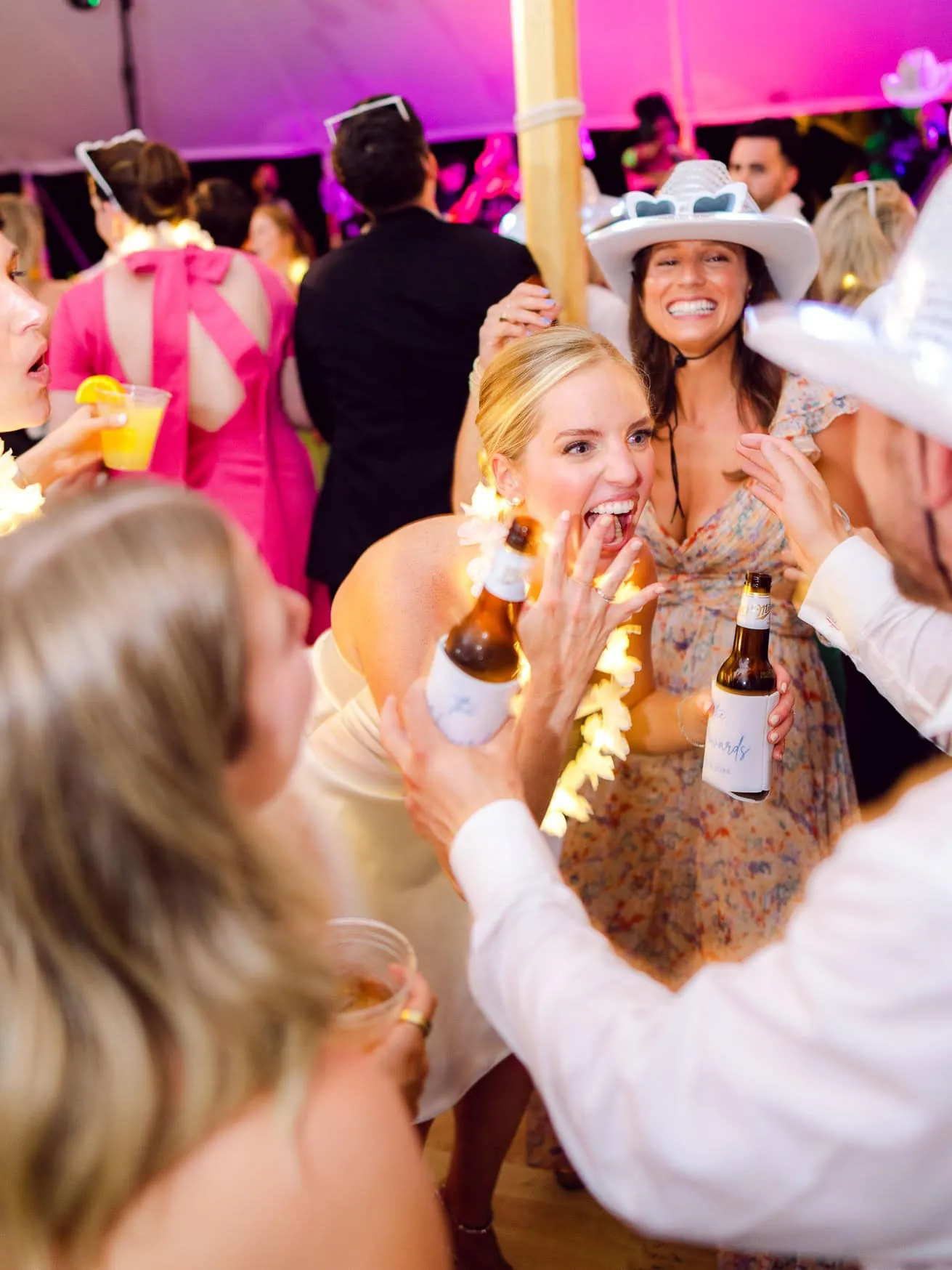 Vibrant wedding reception with guests celebrating, laughing, and drinking beer under colorful lighting. Joyful moments captured during the lively wedding celebration with friends and family.