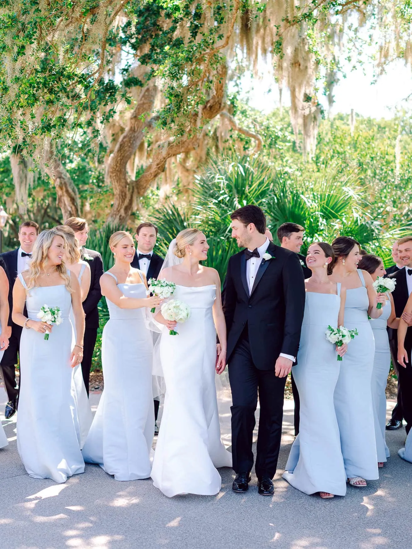 Vow renewal wedding ceremony with bride and groom surrounded by wedding party outdoors in a lush garden setting.