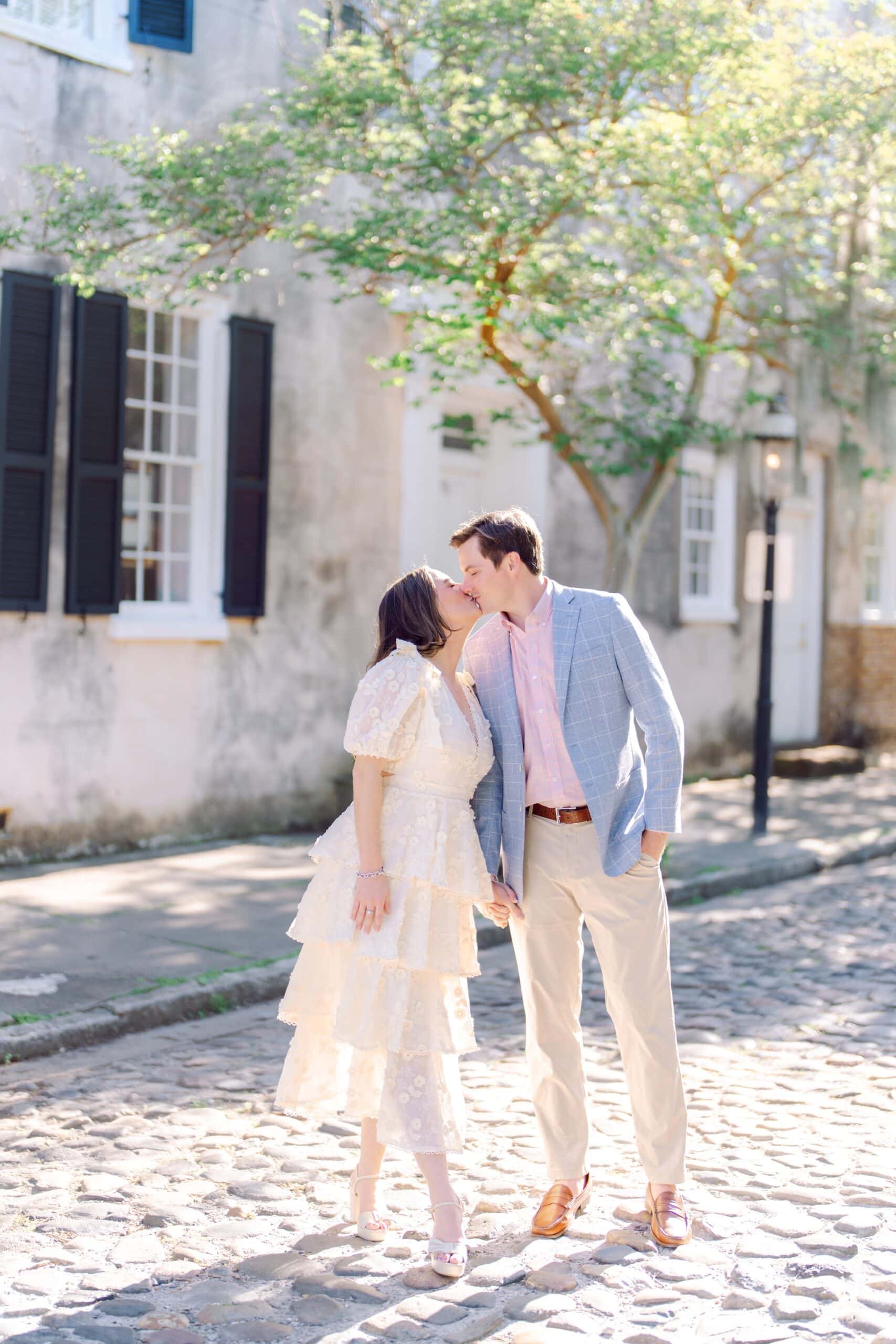 Romantic Charleston SC engagement session with couple kissing on charming cobblestone street near historic homes