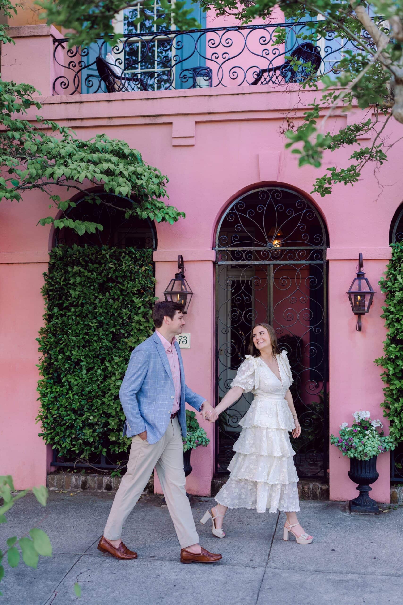 Charming Charleston engagement session with couple in pastel outfits strolling near historic pink house