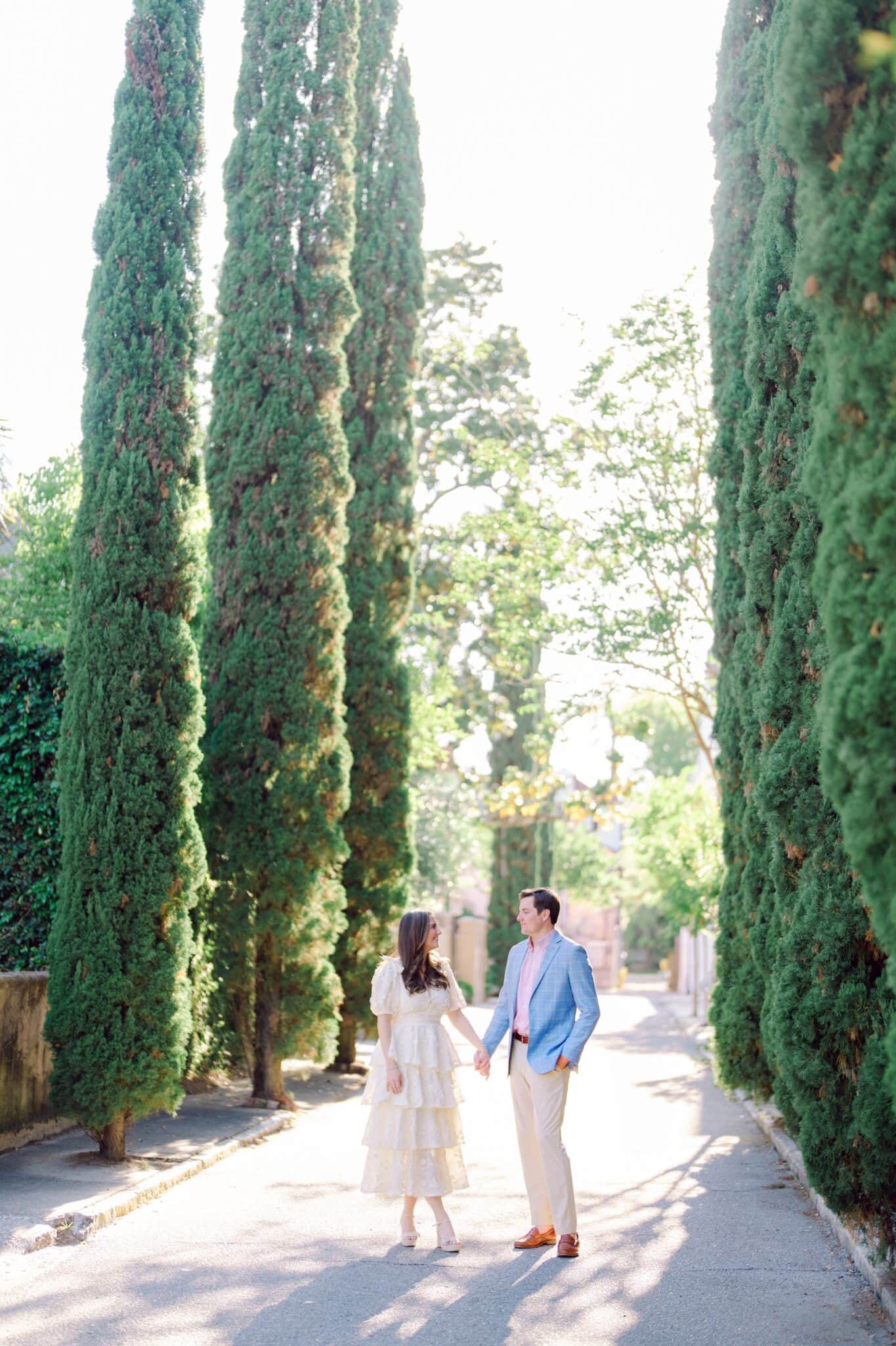 Romantic Charleston engagement photo at iconic Italian-inspired tree-lined path with couple holding hands under tall cypress trees"