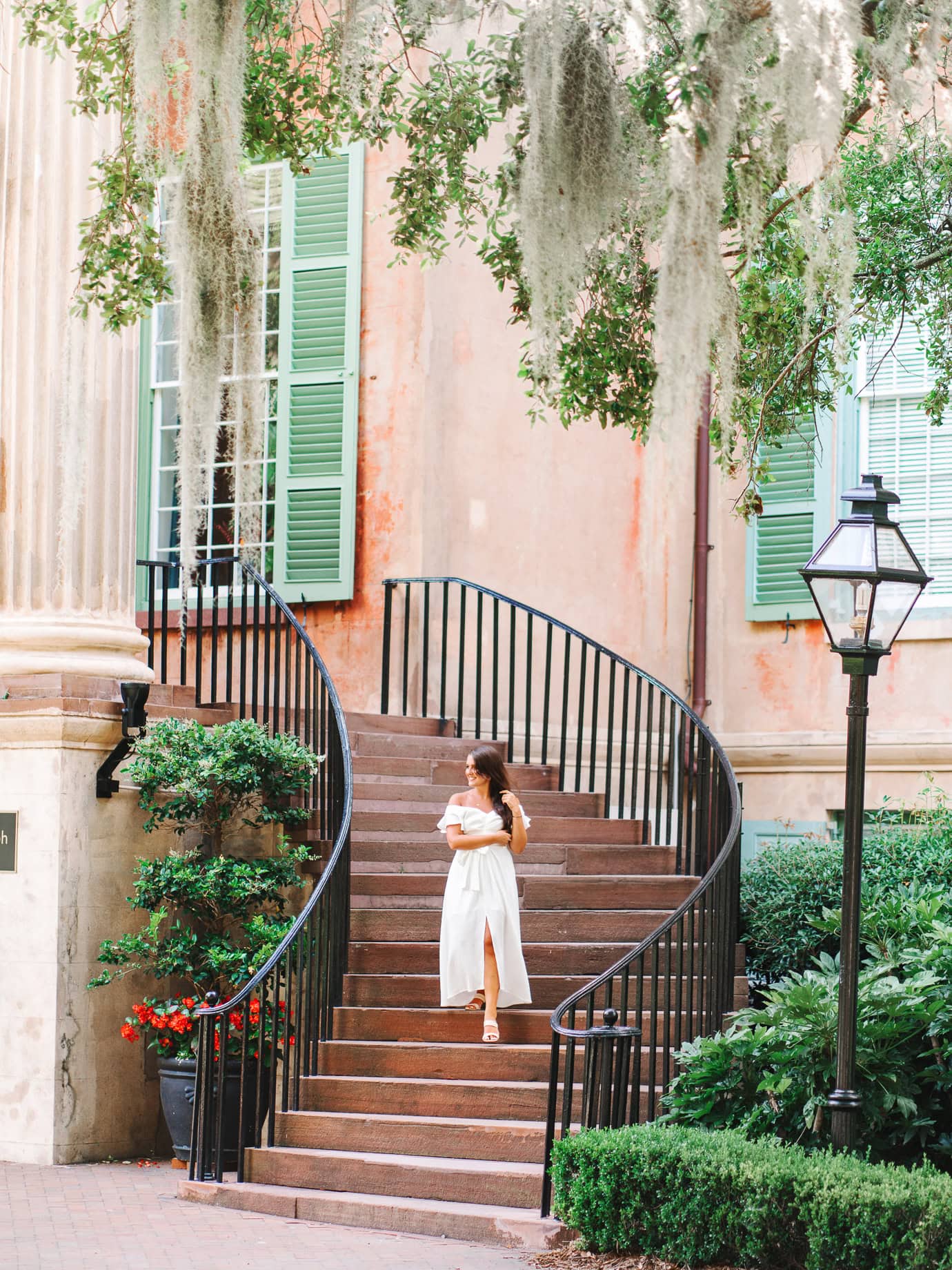 College of Charleston senior walking down iconic spiral staircase with historic columns and green shutters in the background
