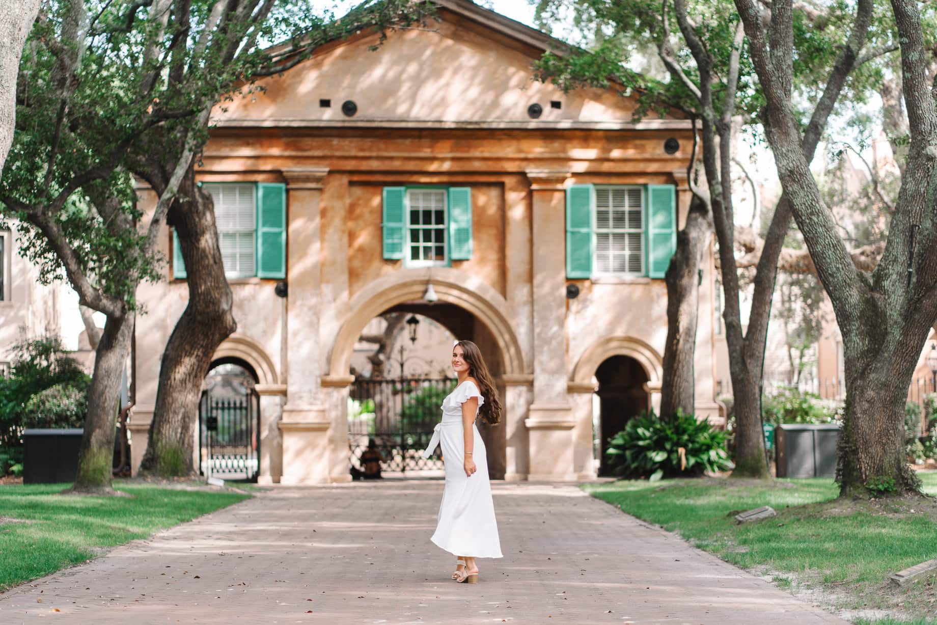 College of Charleston senior walking in front of Randolph Hall with green shutters during graduation portrait session