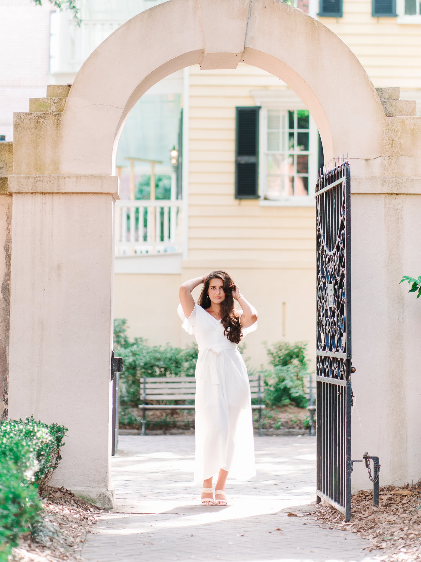 College of Charleston senior standing under stone archway with black iron gate during graduation portrait session