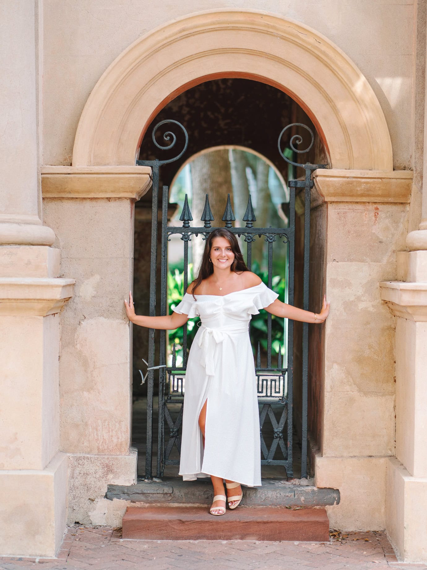 College of Charleston senior posing at the historic wrought iron gate in a white dress during graduation portraits