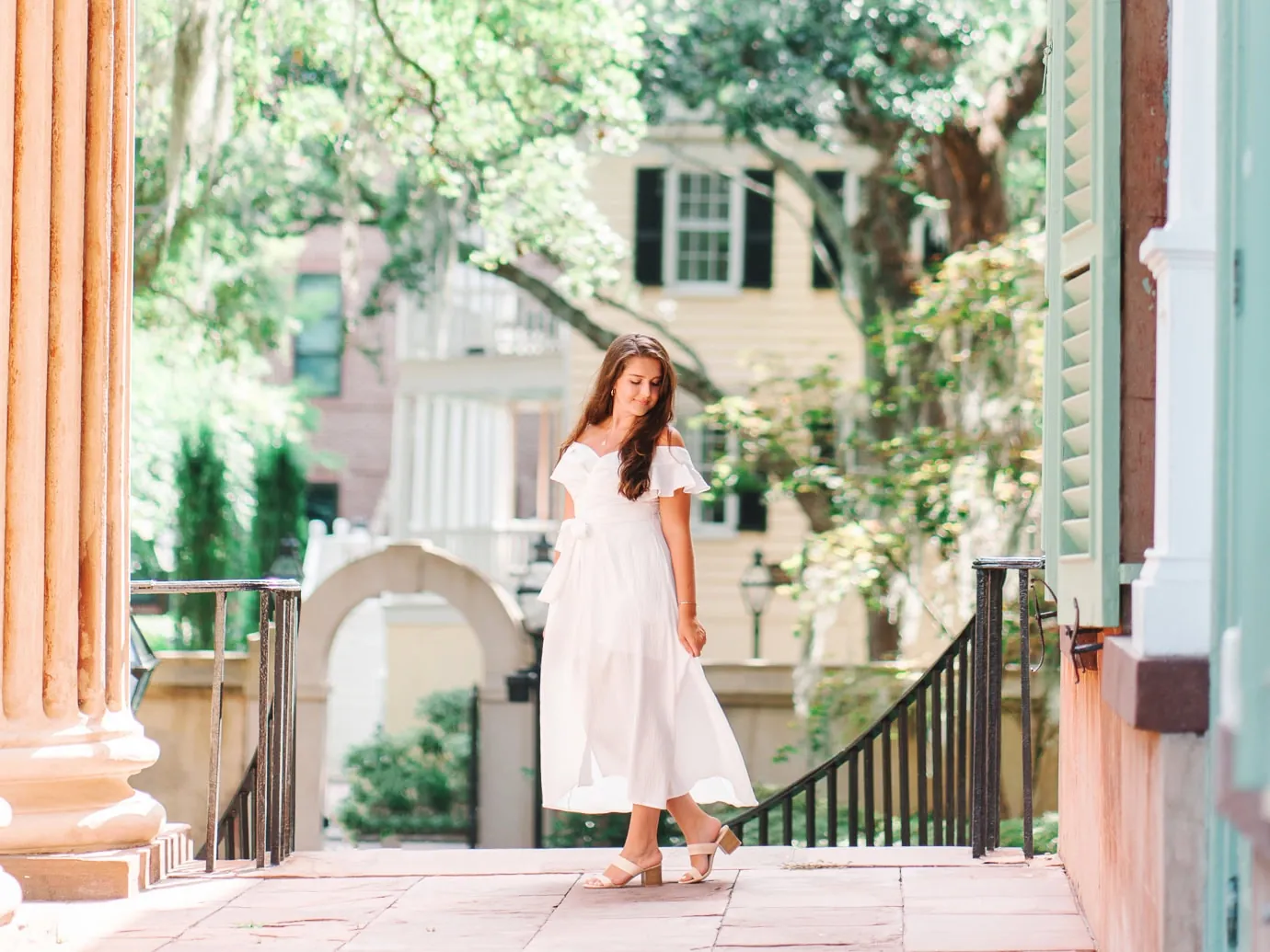 College of Charleston senior walking along brick pathway near columns and arched gate during graduation portrait session