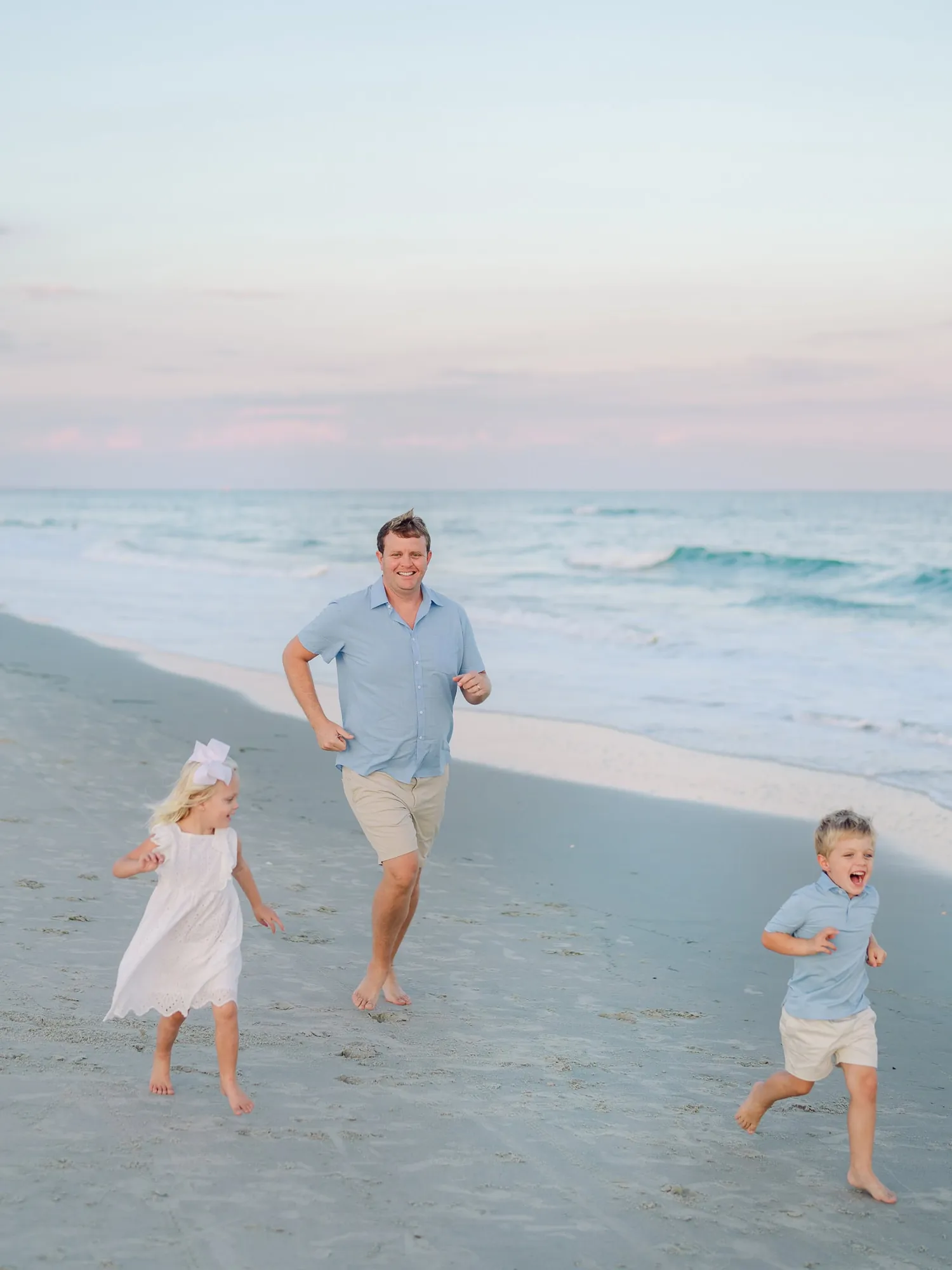 Happy family laughing together at beach during professional photo session, genuine connection moment