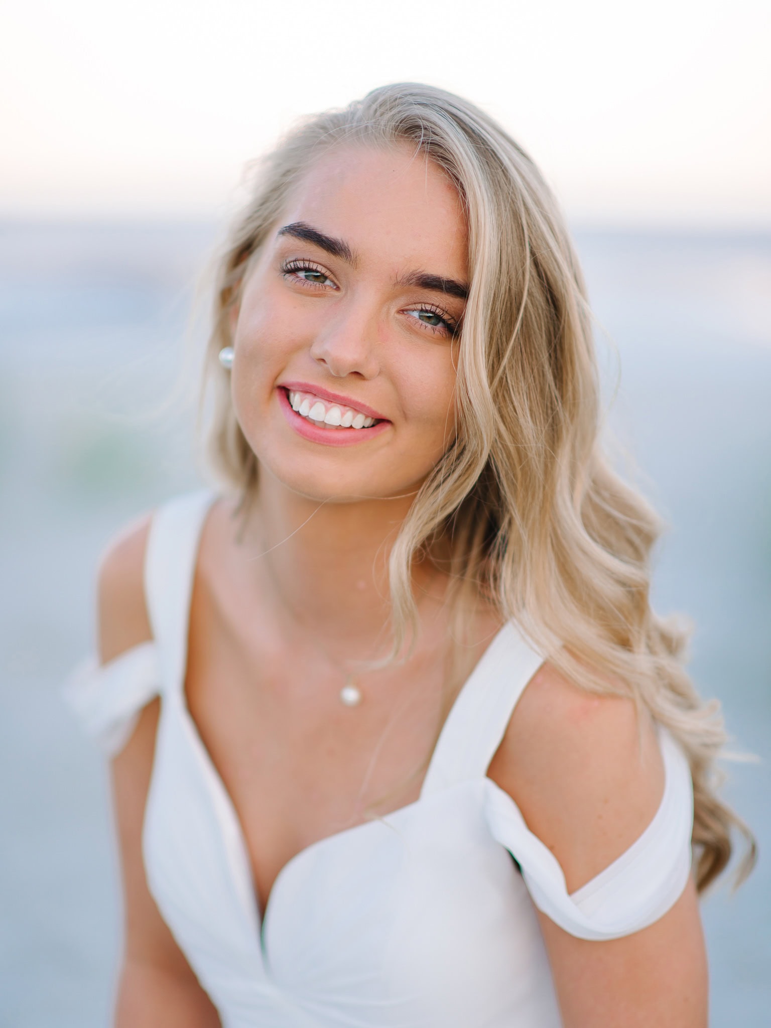 Bright smiling high school senior with blonde hair at the beach during sunset, perfect for senior portrait photography and outdoor family beach portraits.
