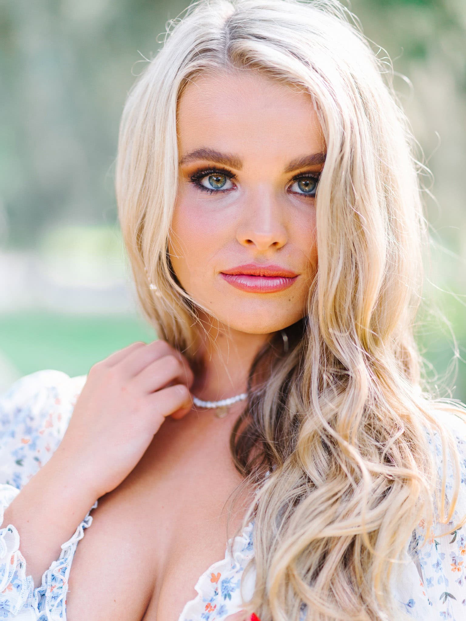 Vibrant portrait of a young woman with wavy blonde hair and bright blue eyes, wearing natural makeup and a delicate necklace, ideal for beach family portraits or senior photography.