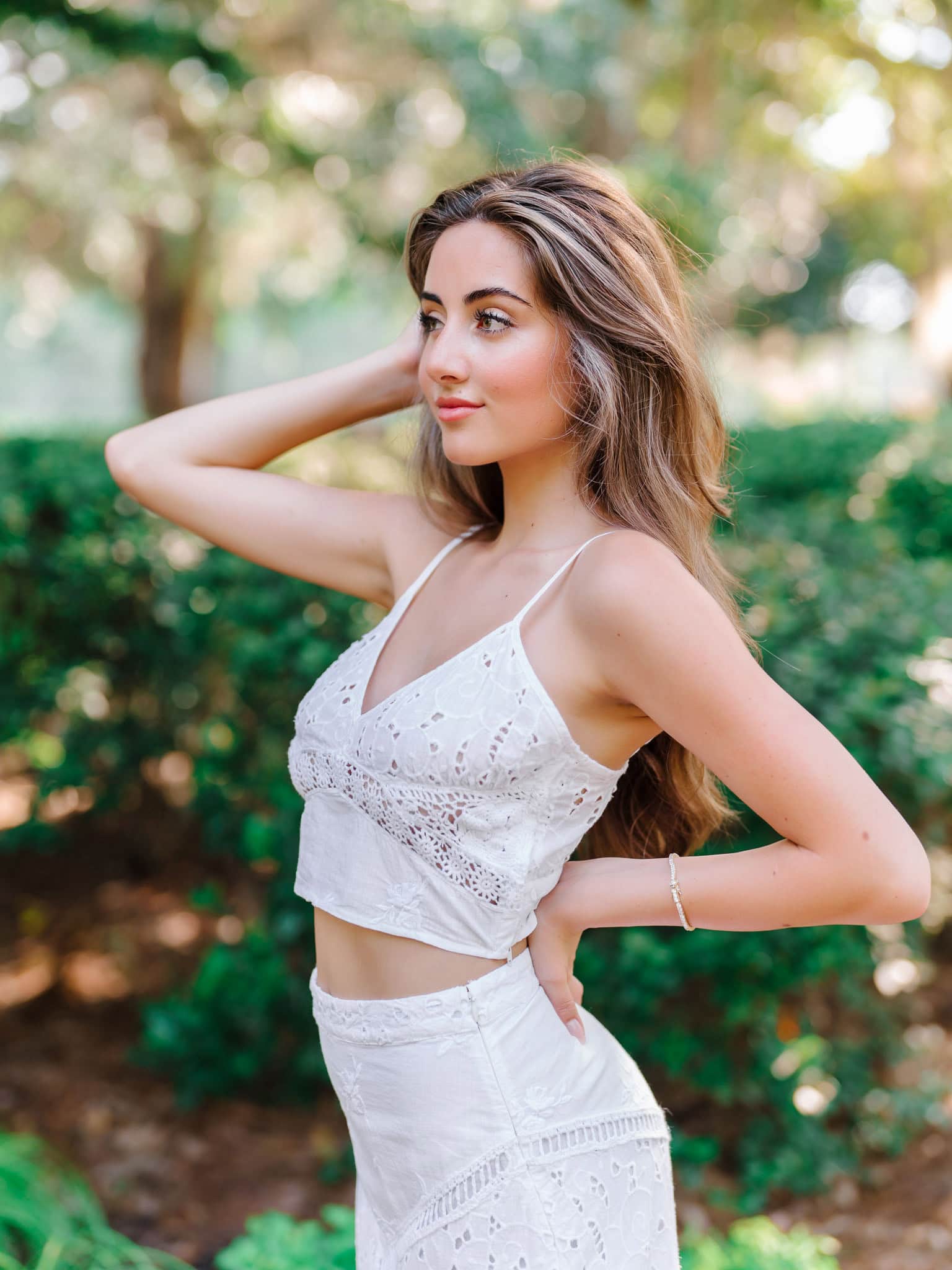 Natural light portrait of a young woman in a white crochet summer dress with a lush green background, perfect for outdoor fashion and summer photography sessions.
