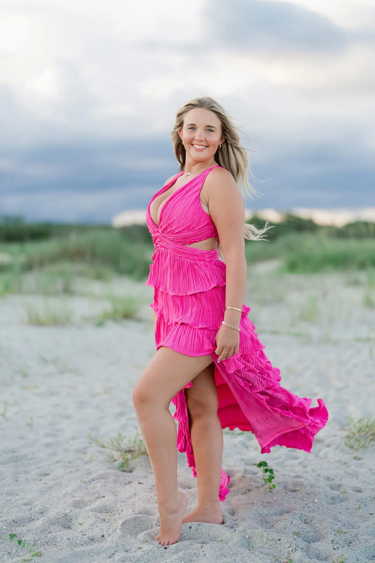 Pink junior prom dress on young woman at the beach in sunset lighting.