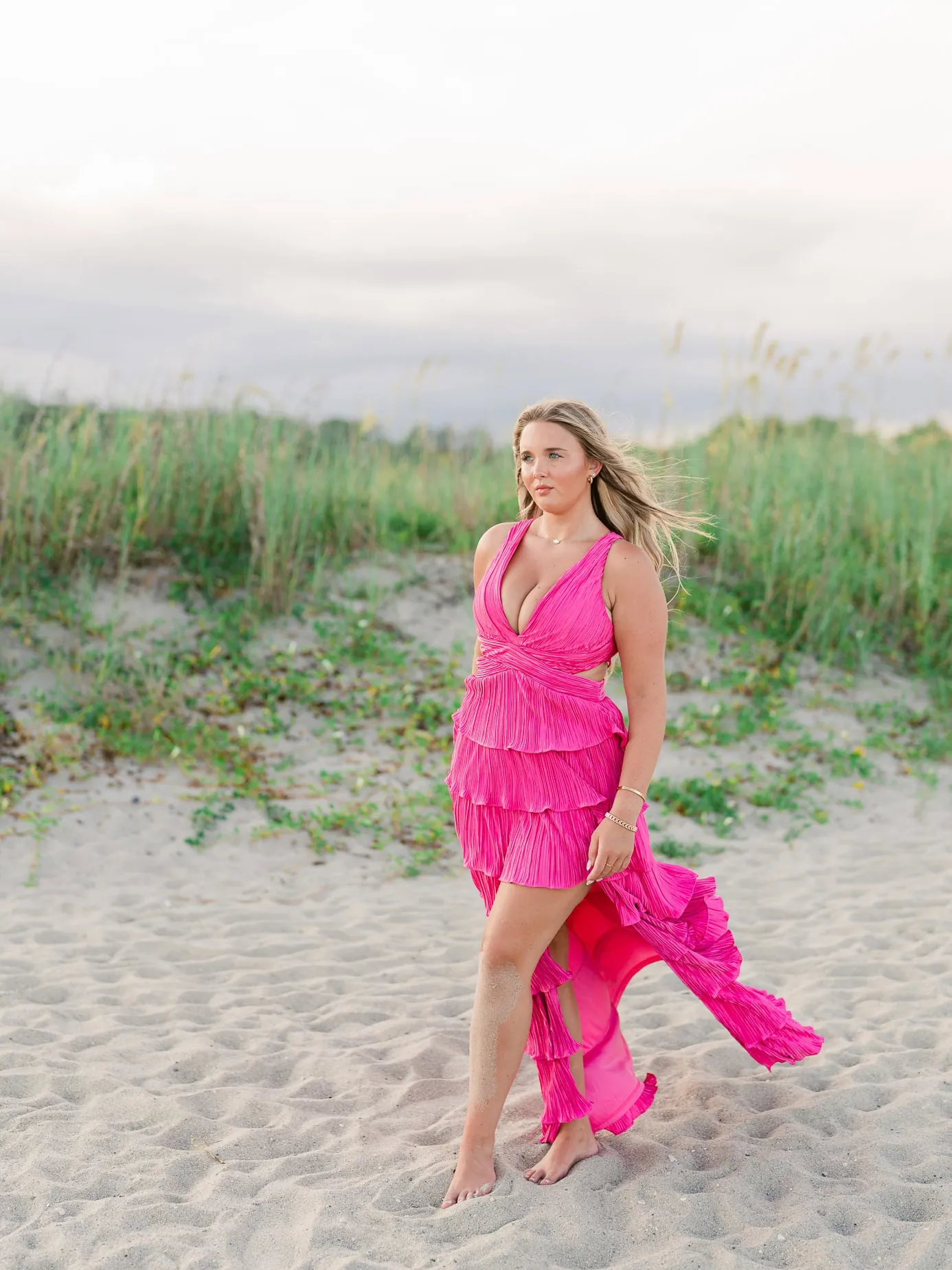 Vibrant pink beach dress worn by a young woman during a beach portrait session with sand dunes and tall grasses in the background.