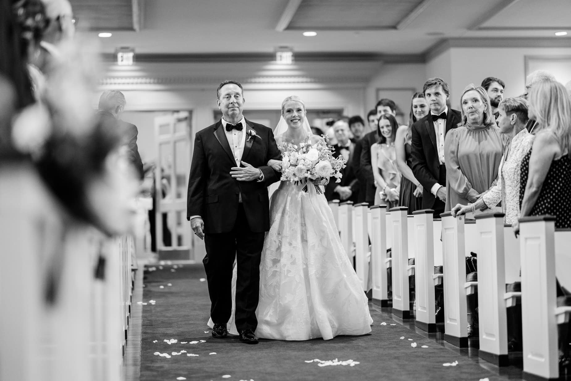Elegant wedding photography capturing a bride walking down the aisle with her father during a joyful ceremony, surrounded by family and friends in a beautifully decorated indoor venue.