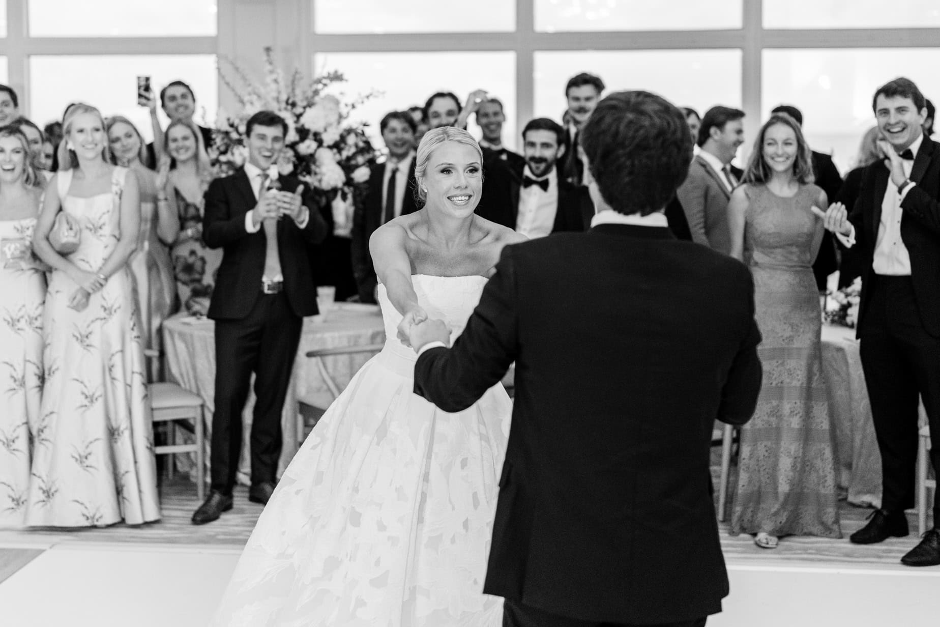 Elegant wedding couple dancing during reception with joyful guests in background, indoor event, celebration, wedding photography, memorable moments.