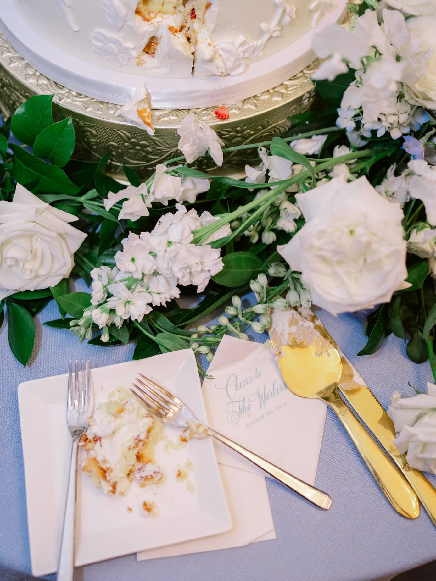 Delicious wedding cake with white frosting, surrounded by elegant white flowers and greenery, on a beautifully decorated table for a wedding celebration.