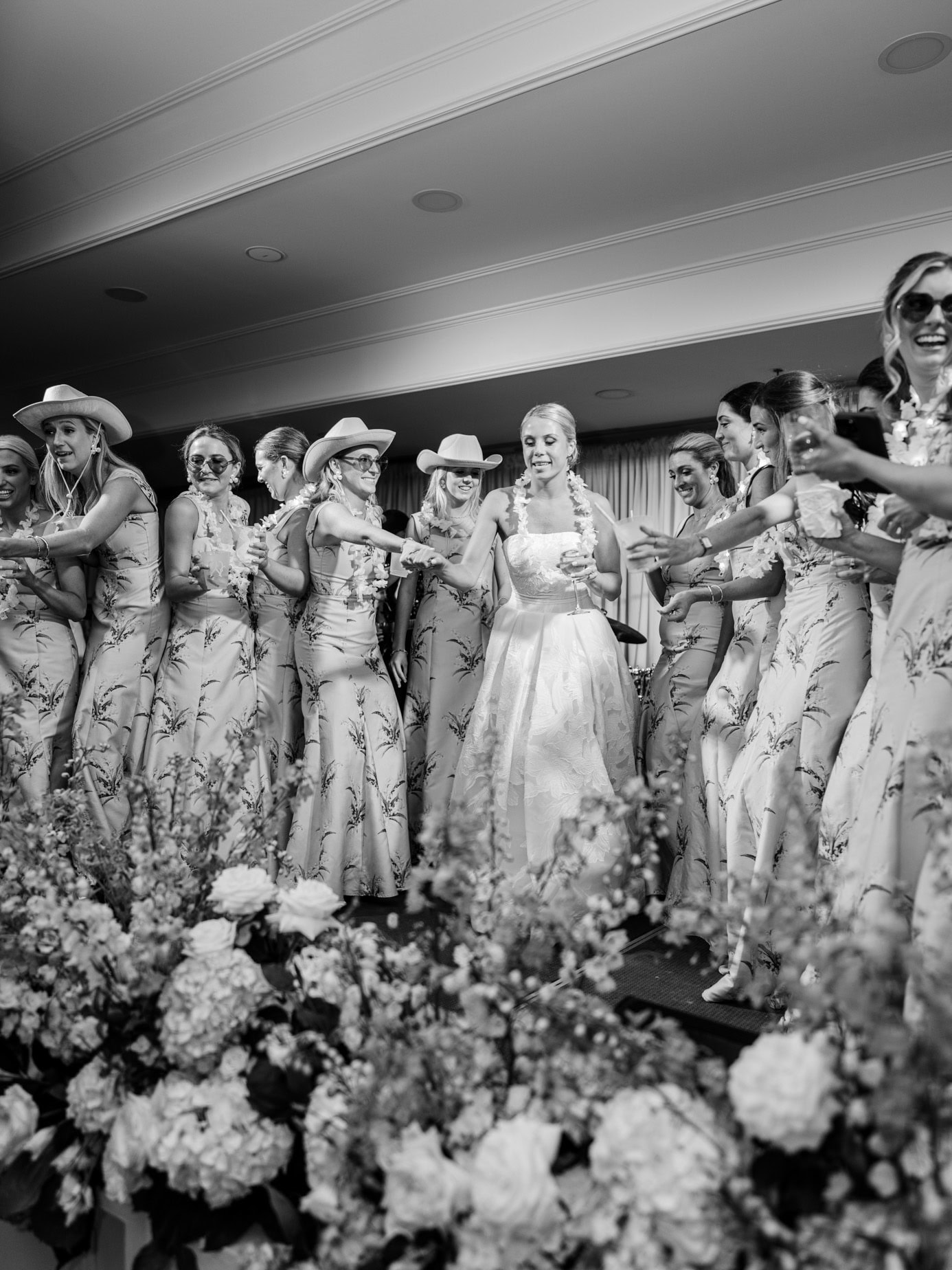 Bridesmaids with floral dresses and cowboy hats at wedding reception, joyful celebration, black and white wedding party photo, elegant bridal event captured by wedding photographer from Pasha Belman.