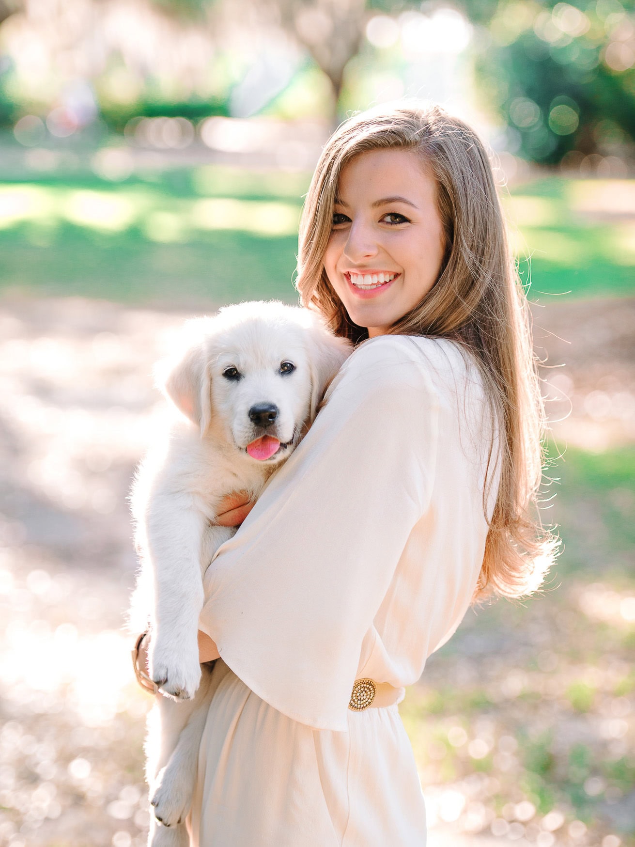 Bright and cheerful young woman holding a cute puppy in a sunlit park for outdoor family and pet portrait photography.