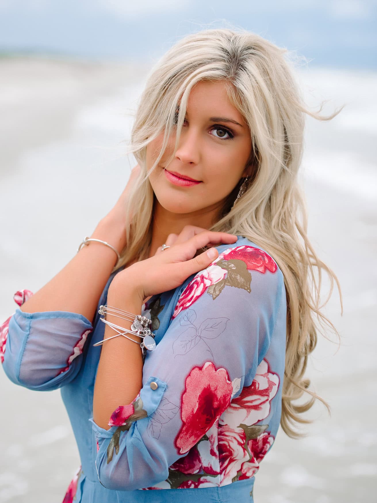 Blonde woman in floral blue dress posing by the beach, portrait showcasing professional wedding and family beach portrait photography.
