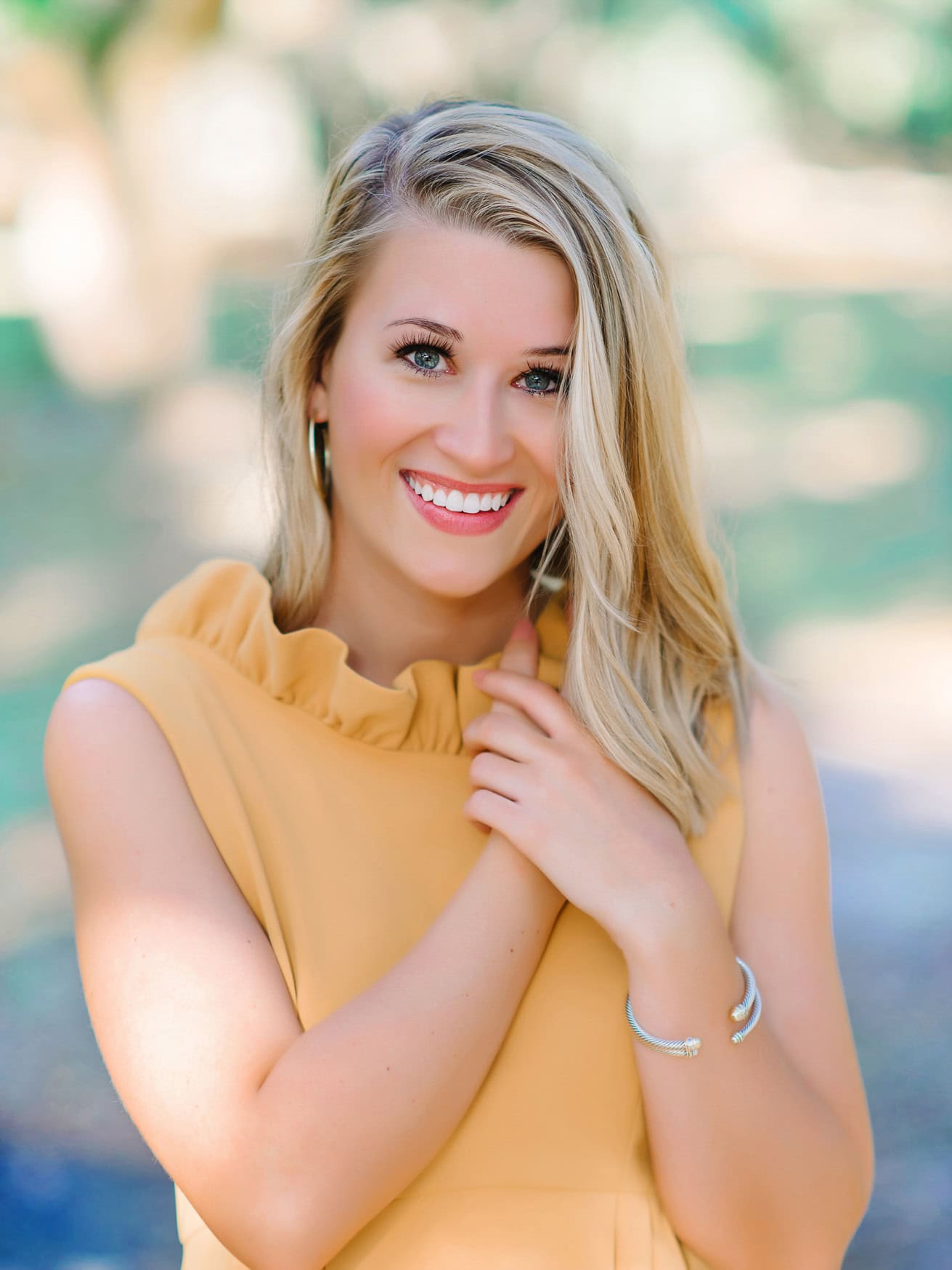 Bright smiling woman in yellow dress with outdoor blurred natural background, portrait photography.