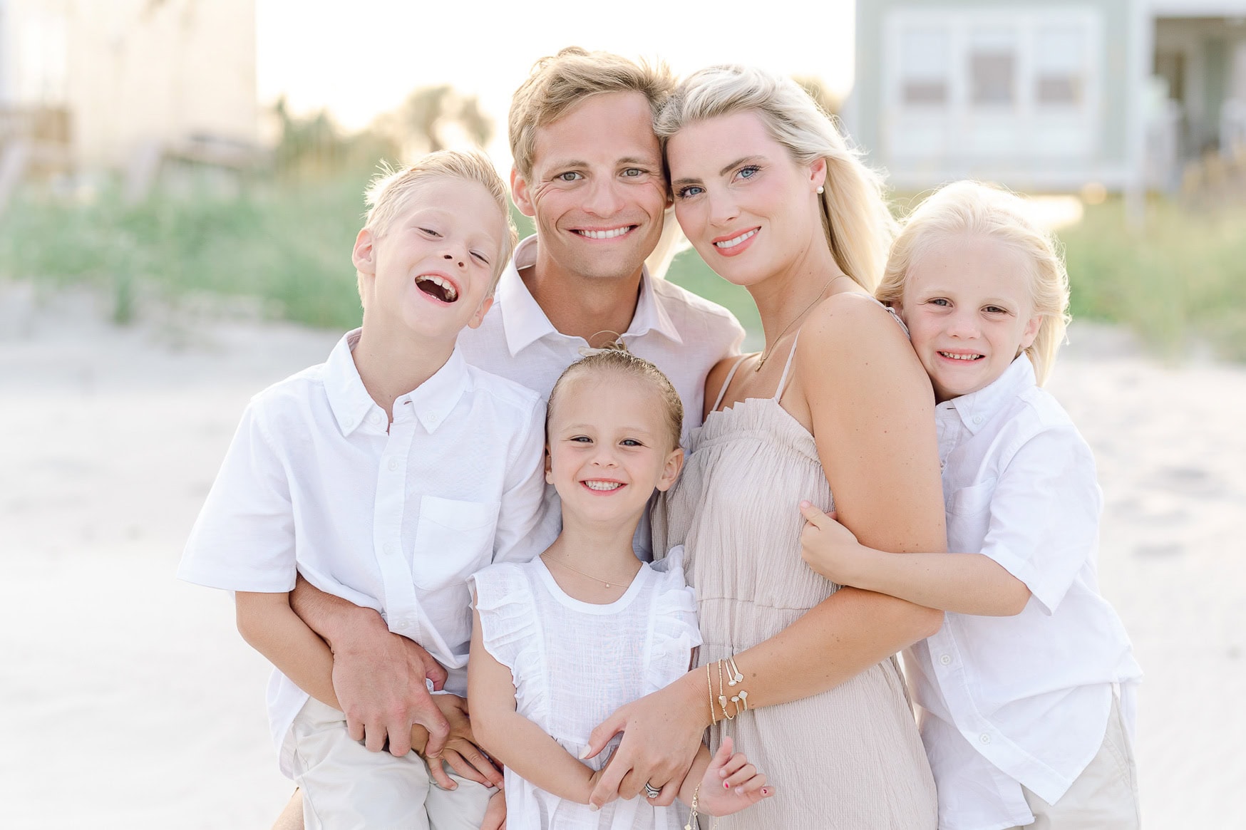 Vibrant family beach portrait featuring mother, father, and three children smiling on sandy shoreline at sunset, capturing joyful family moments and coastal scenery for lifestyle photography.