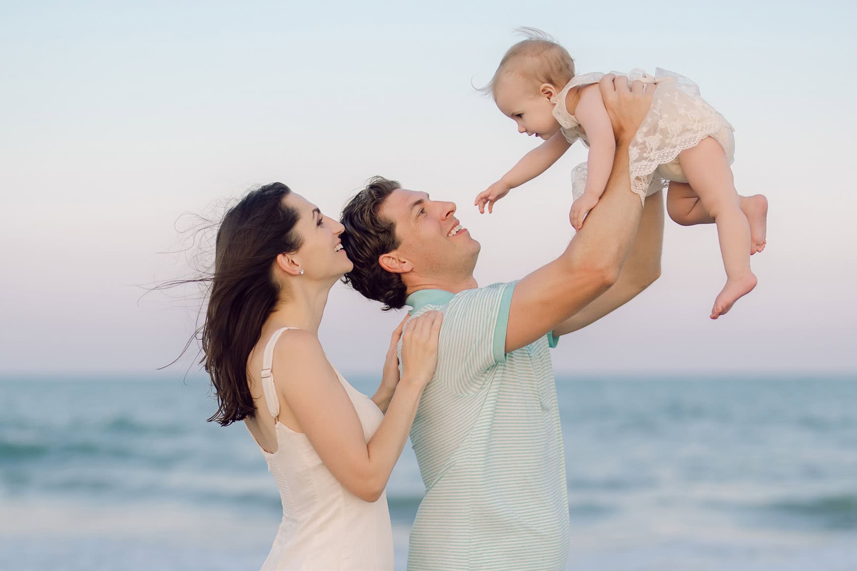 Parents lifting their laughing baby girl at the shoreline during a Murrells Inlet family beach portrait session