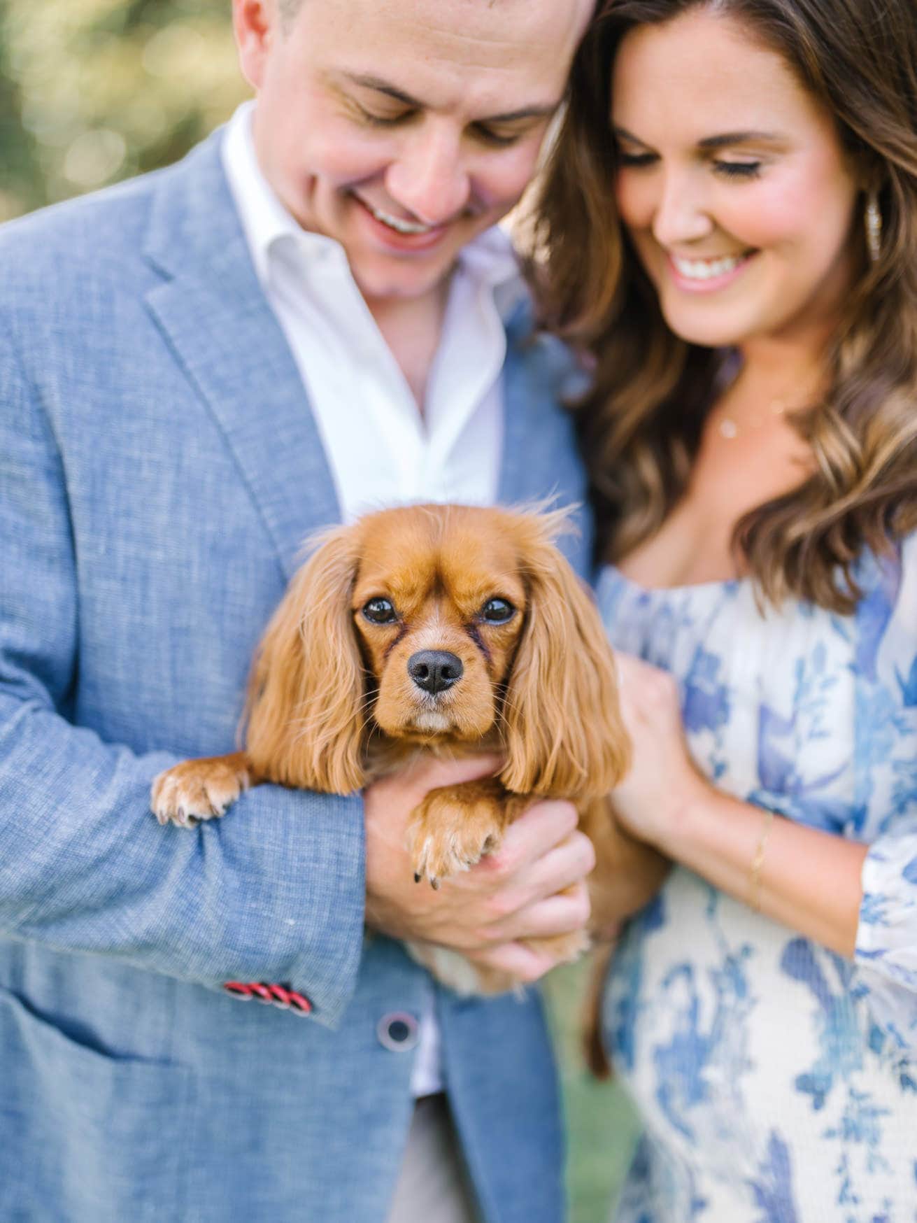 Happy couple holding adorable brown Cocker Spaniel dog outdoors, celebrating their love and furry family member, in a natural light setting.
