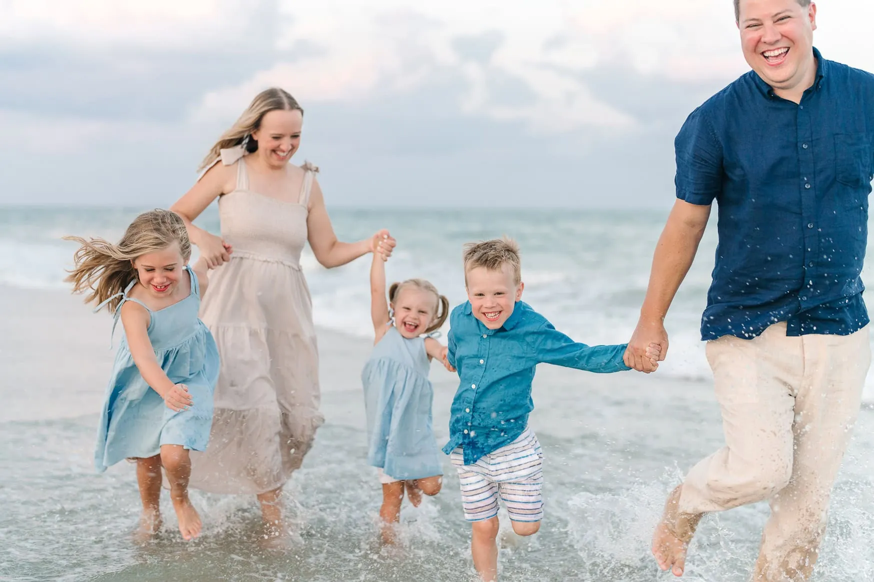 Bright happy family enjoying playful moment at the beach, kids running in the shallow water, parents holding hands, capturing joyful summer family beach portraits, candid fun photo.