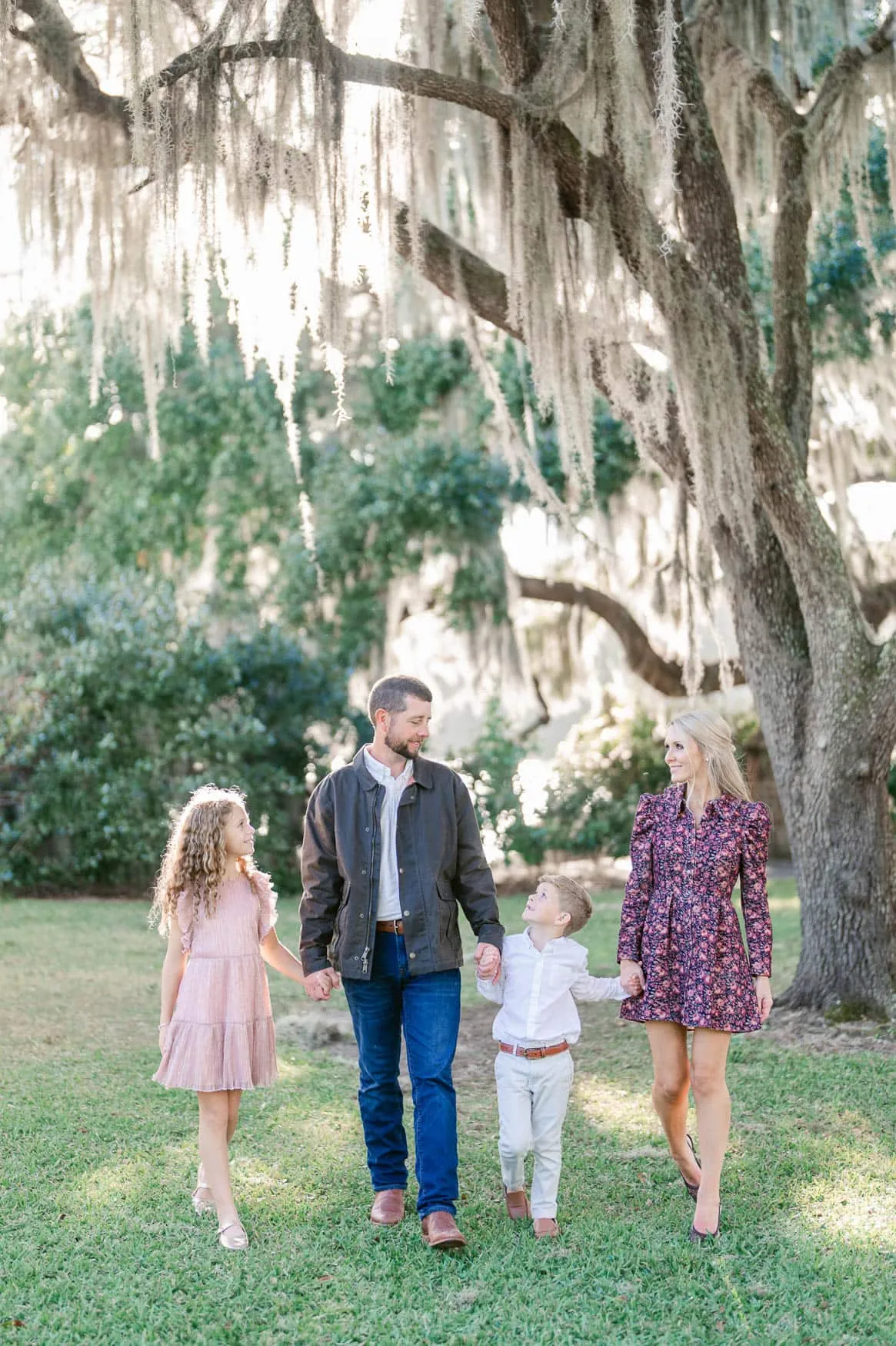 Family walking hand in hand beneath a moss-covered oak tree at Wachesaw