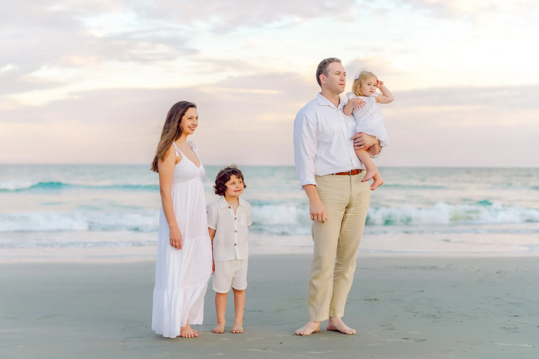 Beach family portrait featuring parents and children walking along the shoreline at sunset