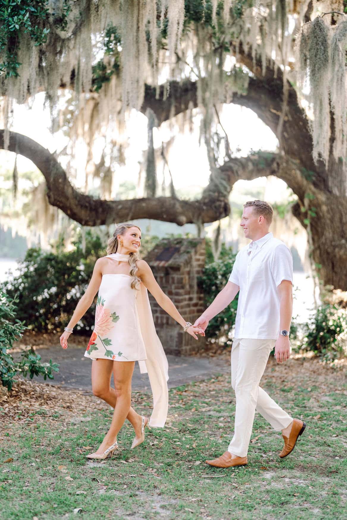 Woman in blush floral mini dress with floor length cape during Pawleys Island live oak engagement session