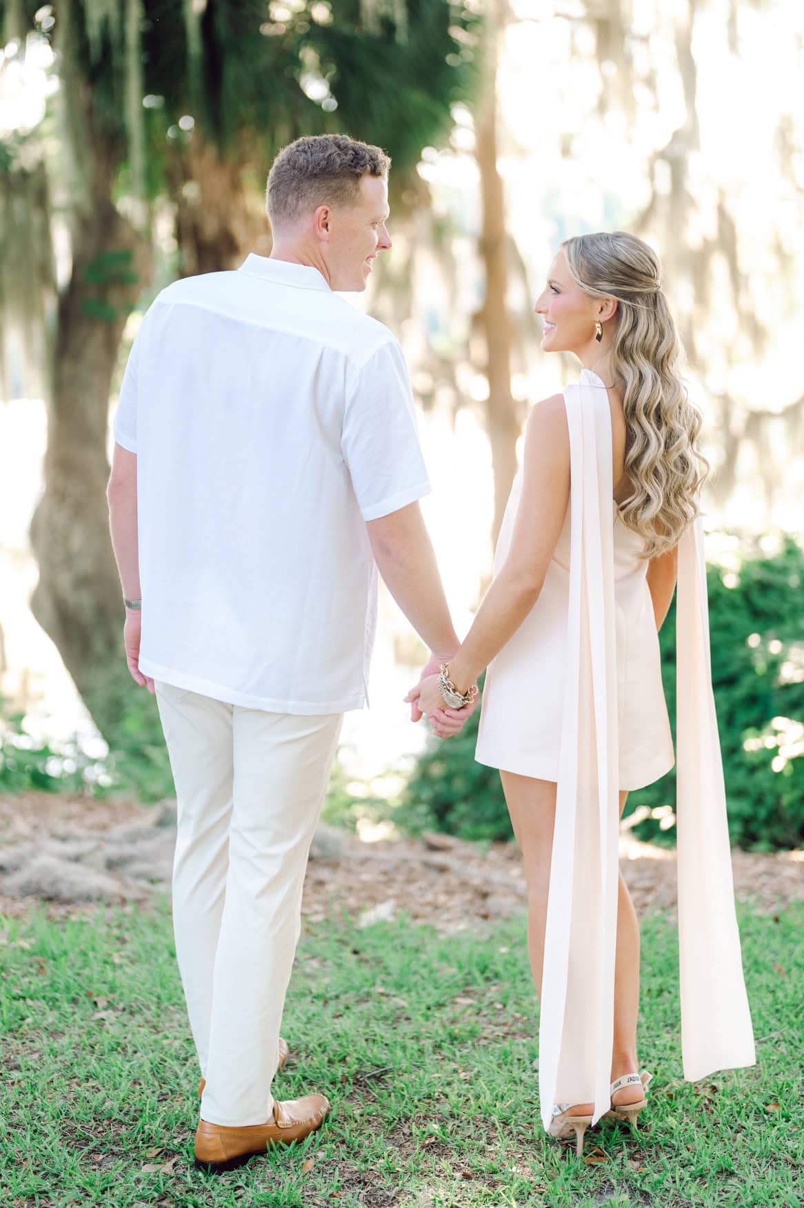 Couple walking hand in hand under Spanish moss live oaks during their Pawleys Island engagement session photographed by Pasha Belman