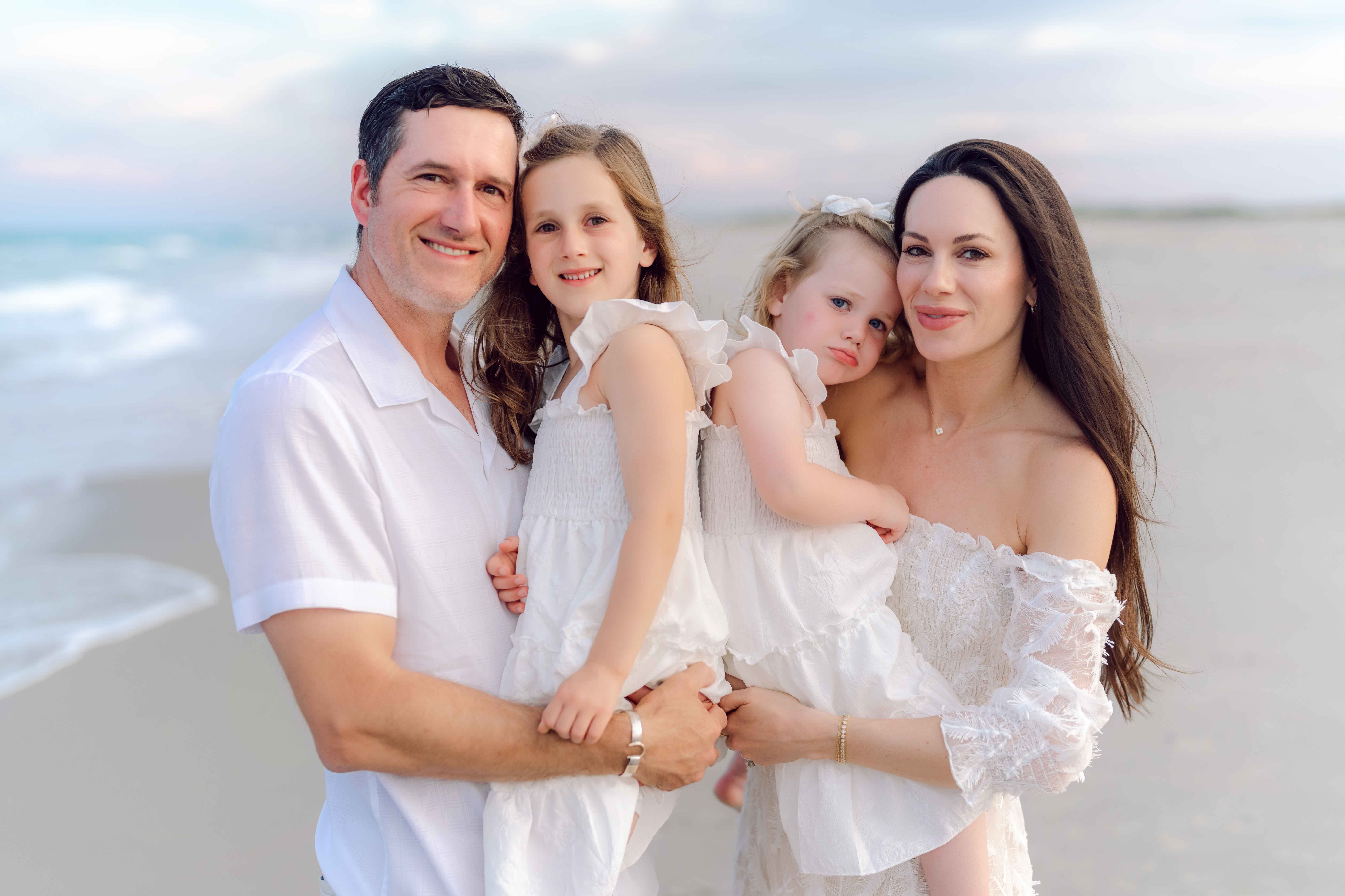Parents standing together while their daughters play on the beach in Pawleys Island.