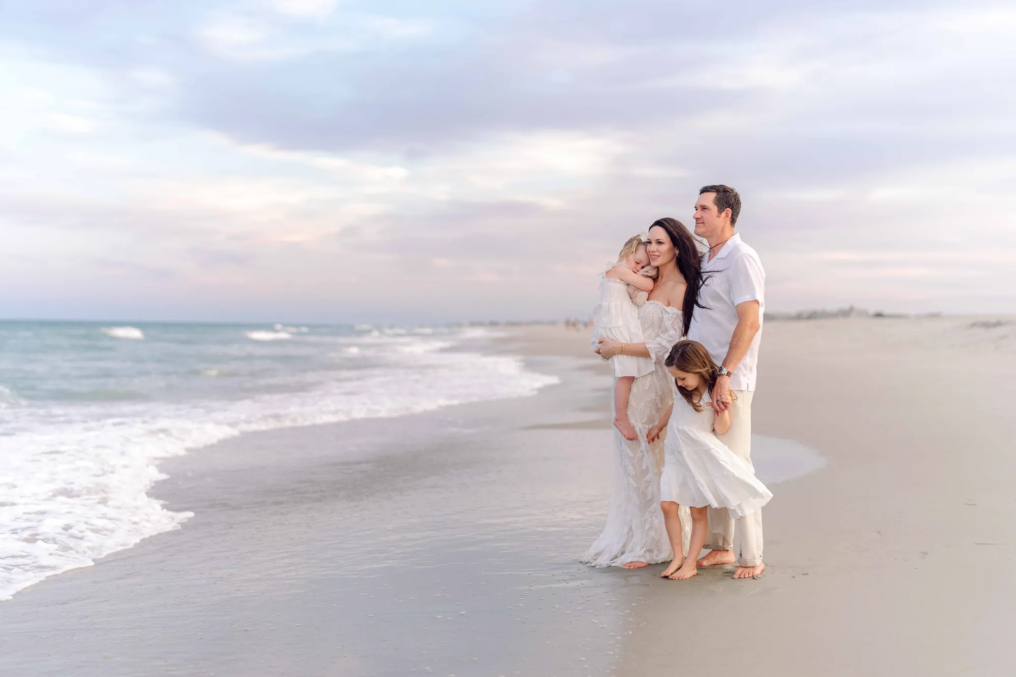 Family of four standing together on the beach in Pawleys Island at sunset.